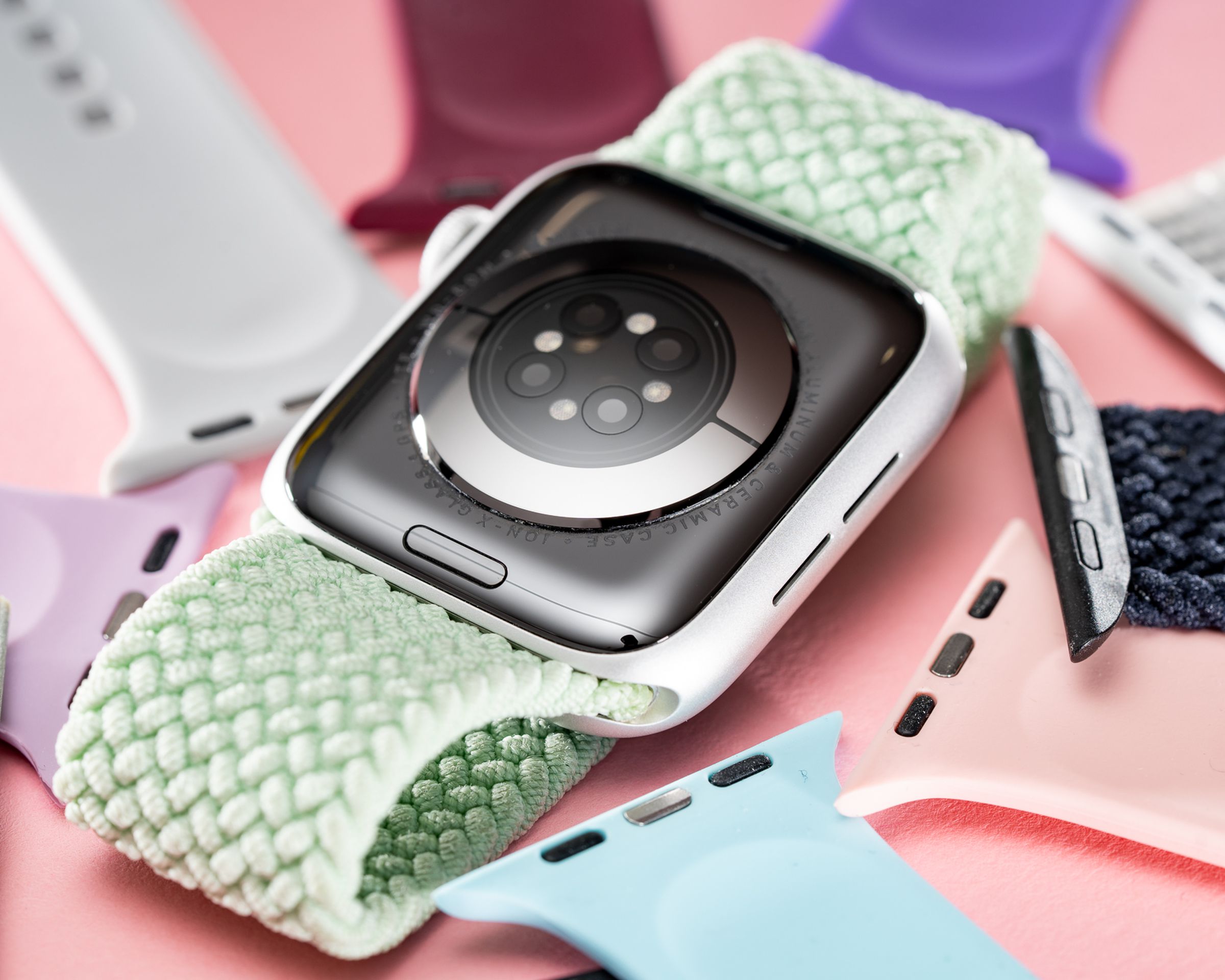 An upturned Apple Watch surrounded by spare straps, with its hidden band release button displayed prominently.
