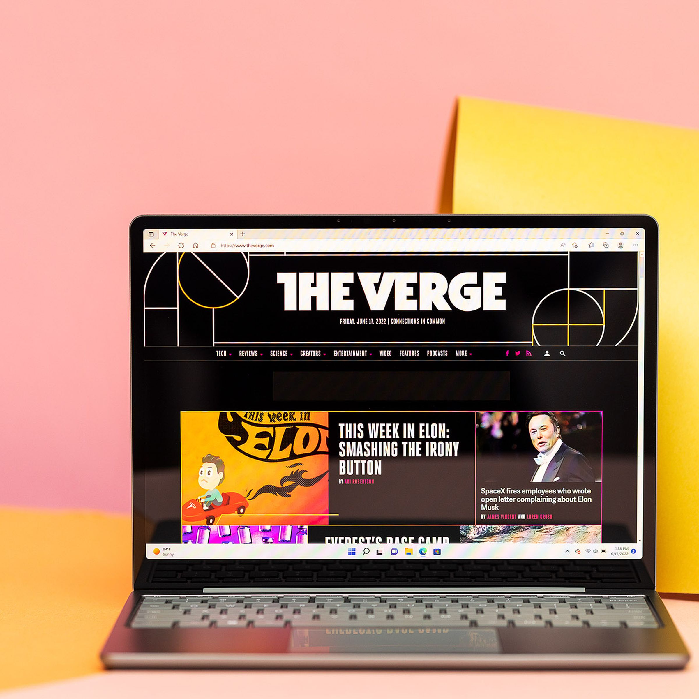 A sage-colored Microsoft Surface Laptop Go 2 with its screen open and facing the viewer in front of a pink and yellow backdrop.