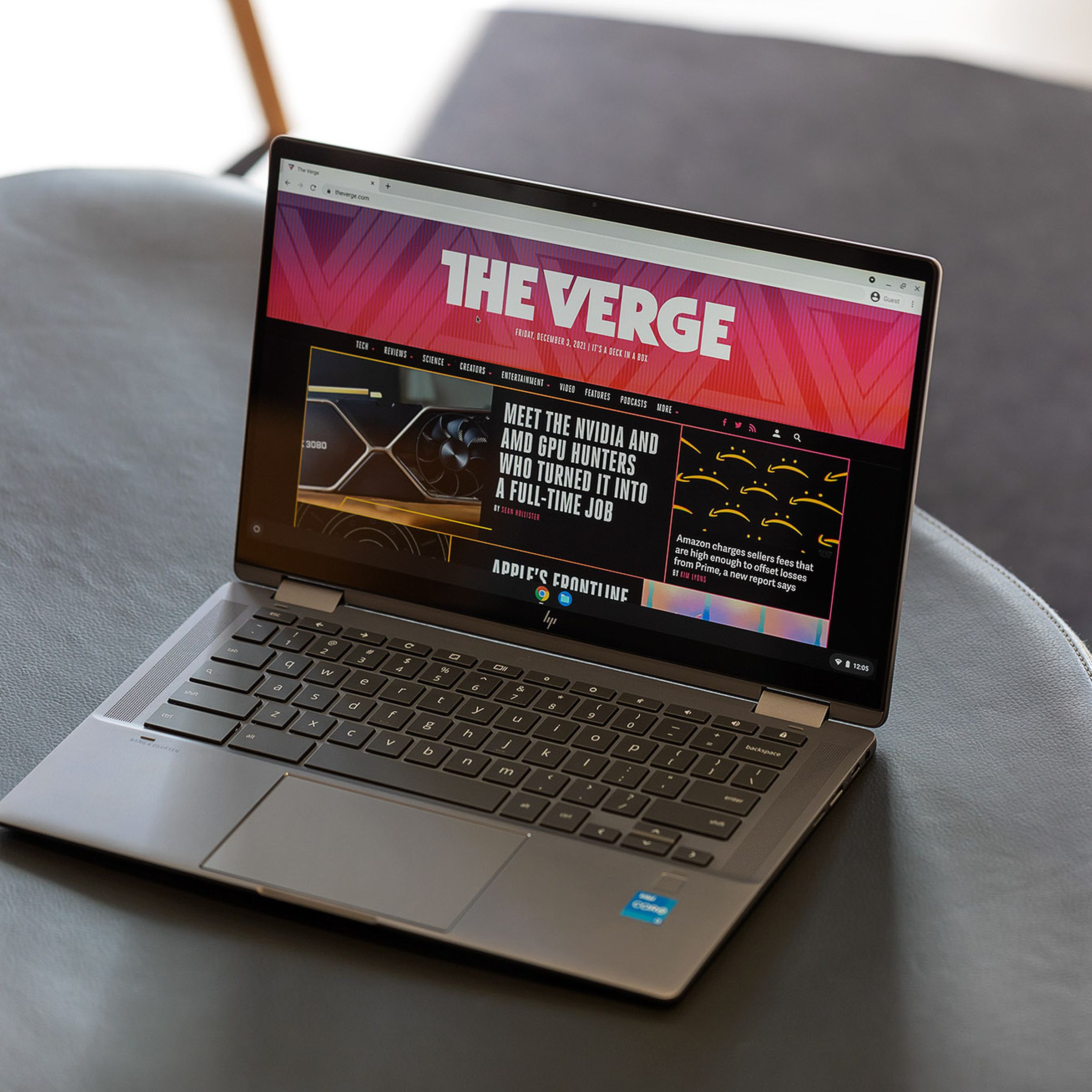 The HP Chromebook x360 14c open on a gray bench seen from above and to the right. The screen displays The Verge homepage.