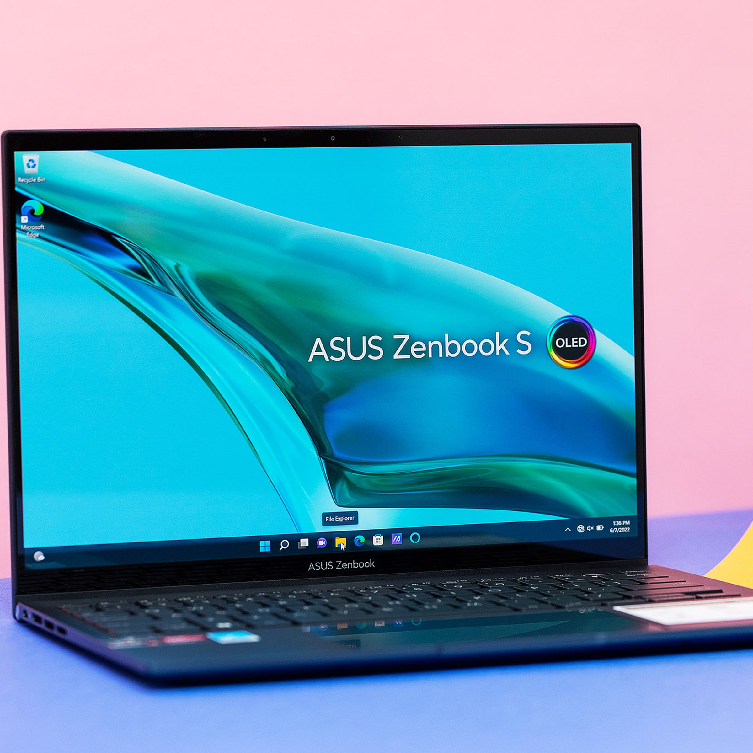 The Asus Zenbook S 13 OLED on a blue and pink background. The screen displays a stream of water on a blue background with the Asus Zenbook S OLED logo.