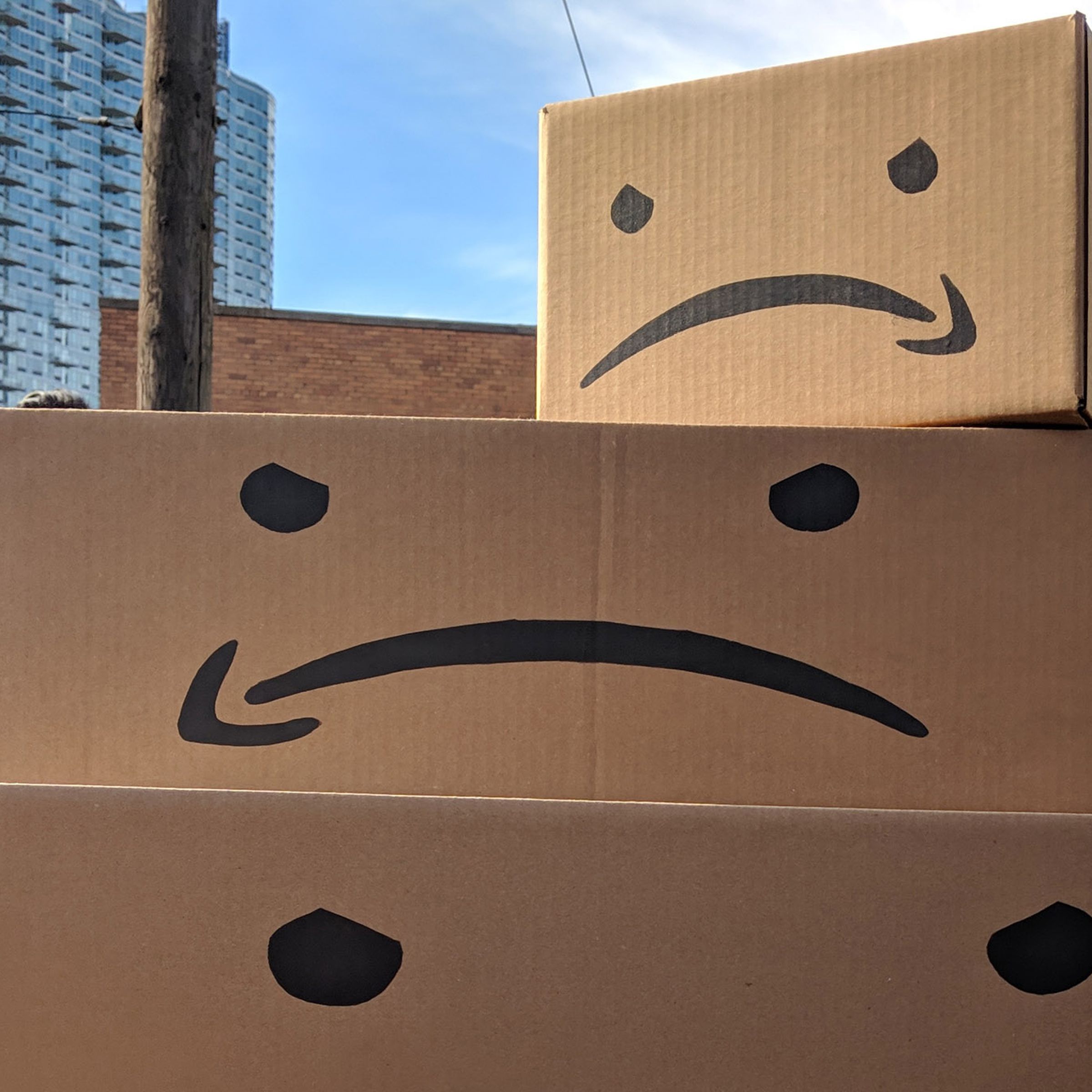 Image of three cardboard boxes stacked on top of each other, with frowning faces using an upside-down amazon logo for the mouth printed on them.