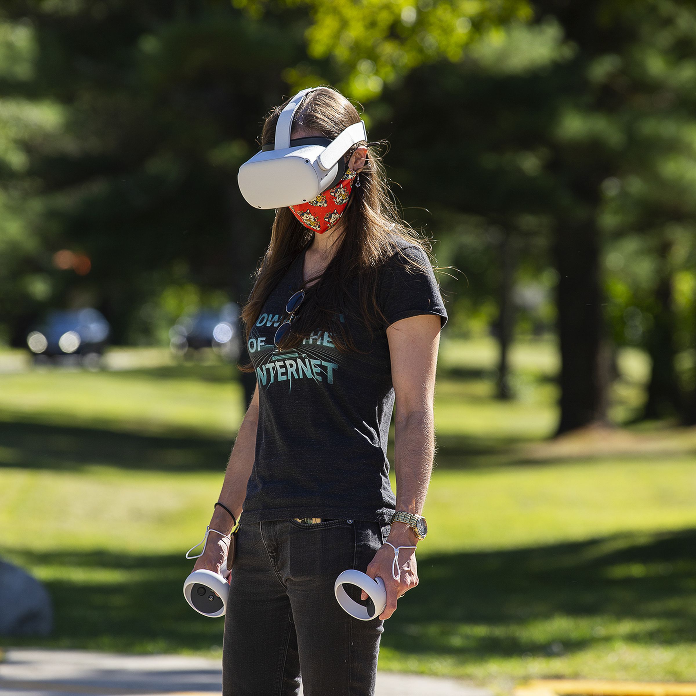 Photo of a person standing in a parking lot wearing a white virtual reality headset and holding two controllers in their hands.