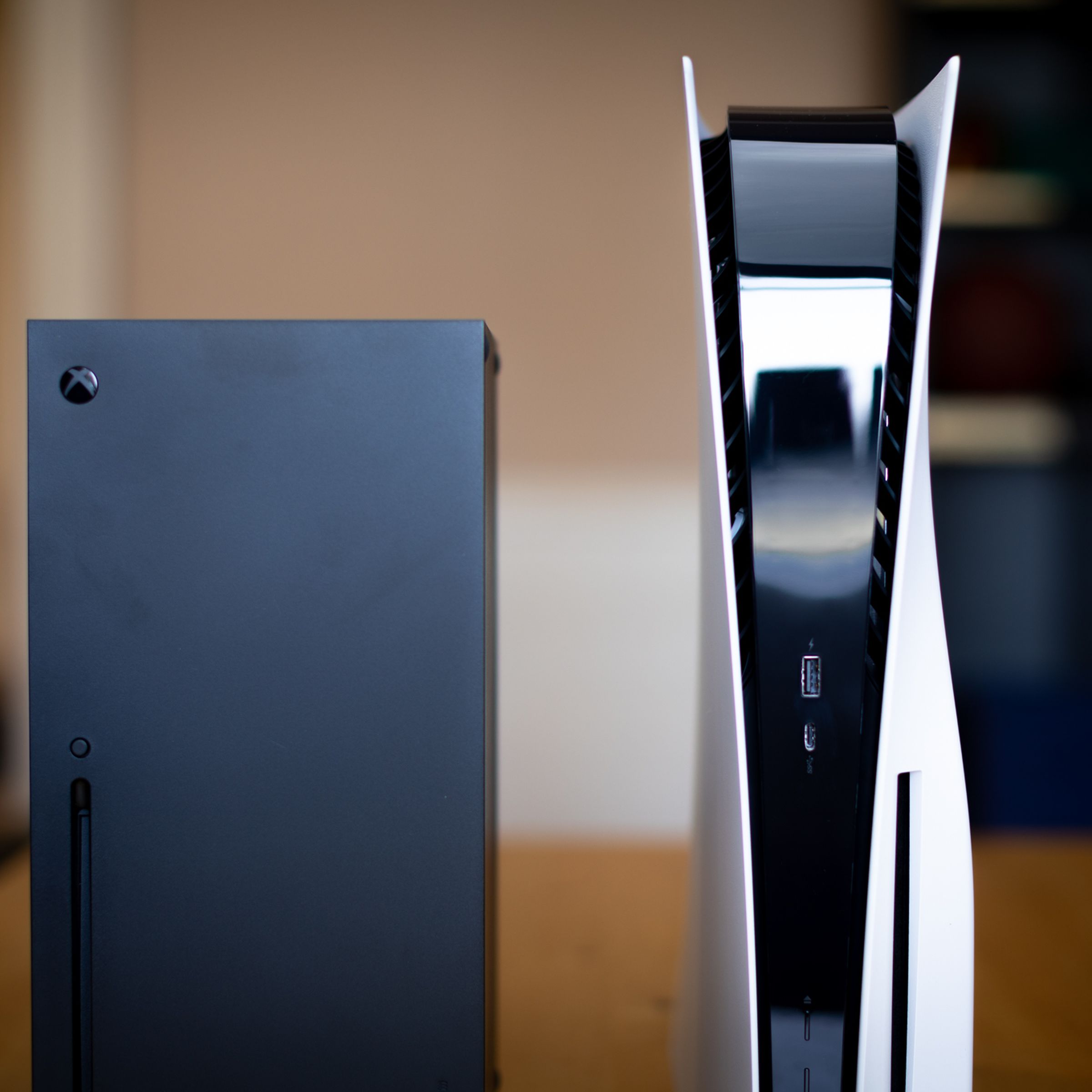 The Xbox Series X and PlayStation 5 standing side-by-side on a. table.