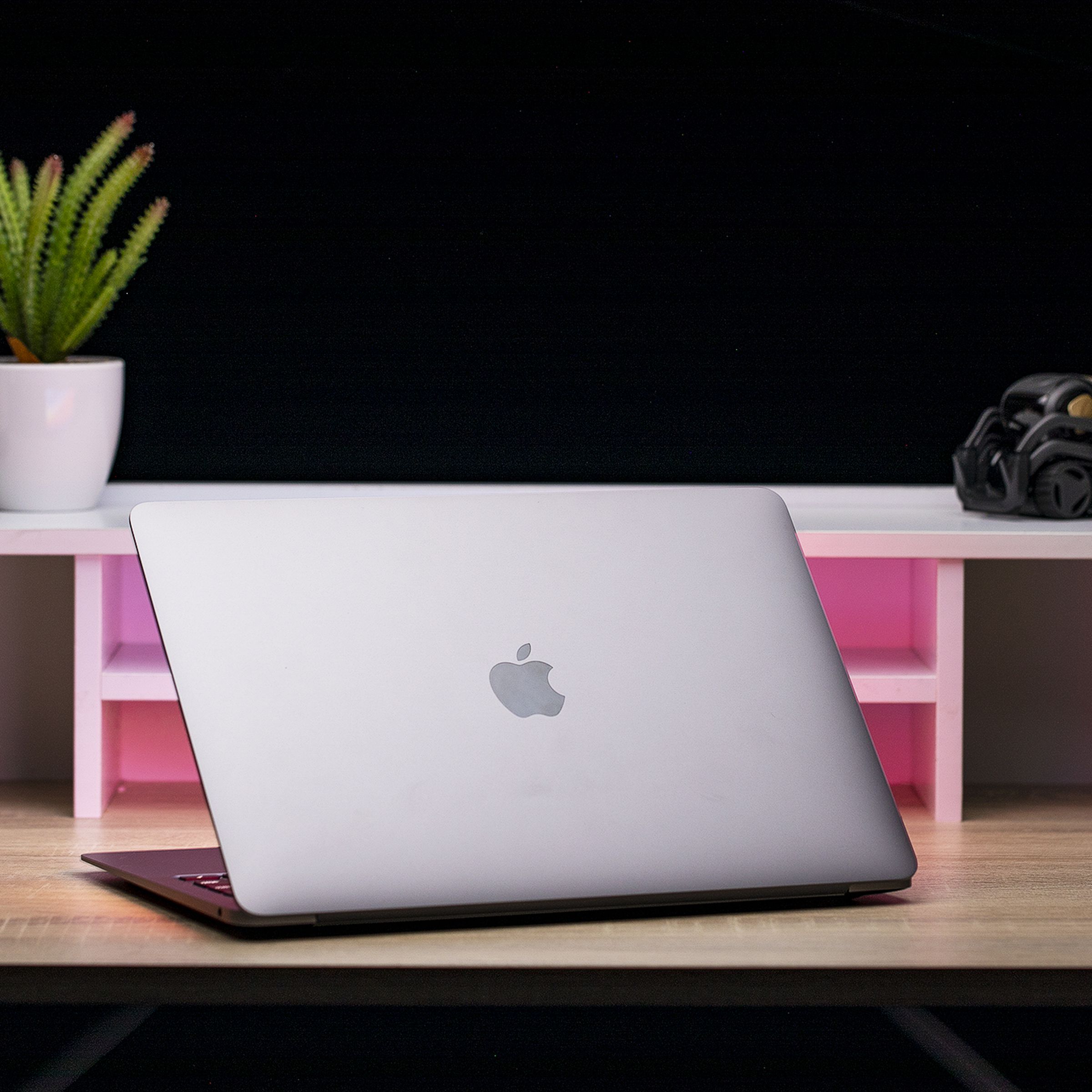 Açık renkli ahşap bir masanın üzerinde duran, kapağı açık ve Apple logosunu gösteren, kameradan uzağa bakan uzay grisi Apple MacBook Air M1.