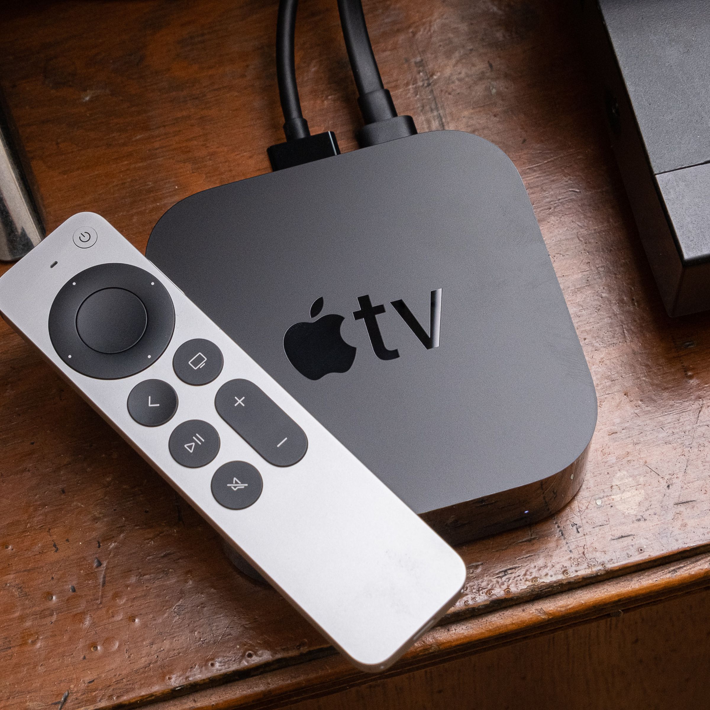An Apple TV from 2021 and its Siri Remote sit on top of a wooden entertainment center.