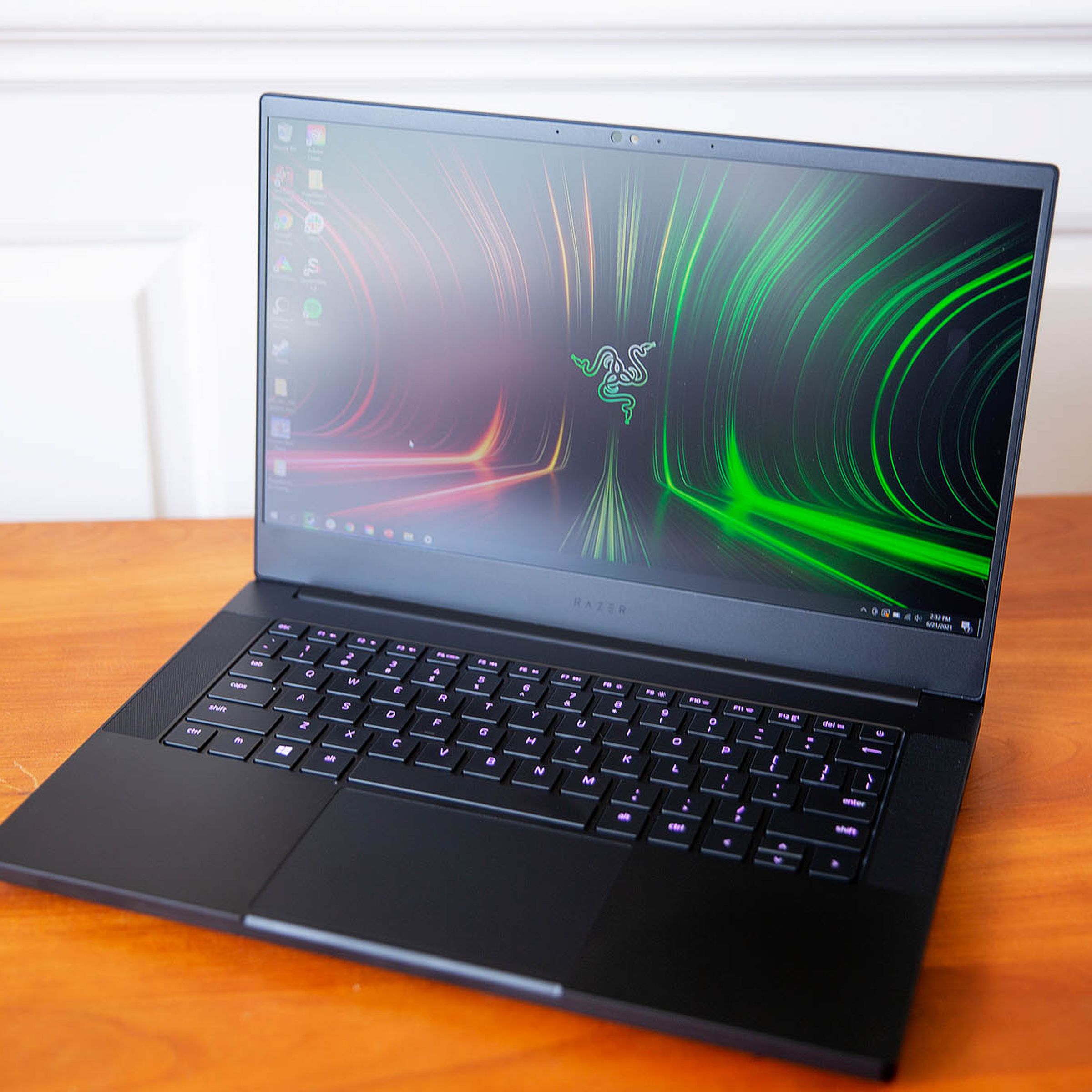 The Razer Blade 14 seen from above, open, angled to the left. The screen displays the Razer logo on a red and green background. The keys are lit a dark pink.