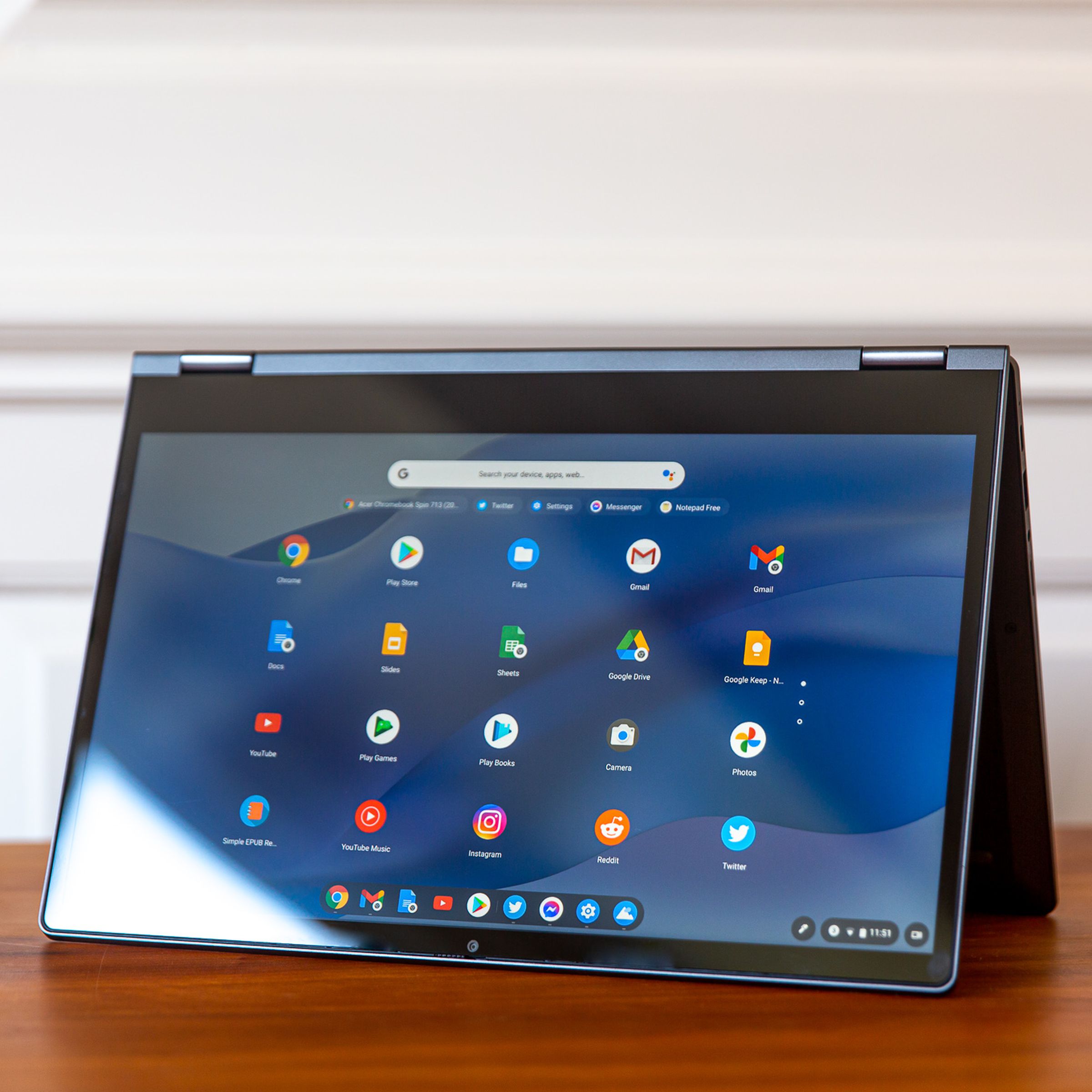 The Lenovo Flex 5 Chromebook in tent mode, angled to the left. The screen displays a grid of Chrome OS icons on a blue wavy background.