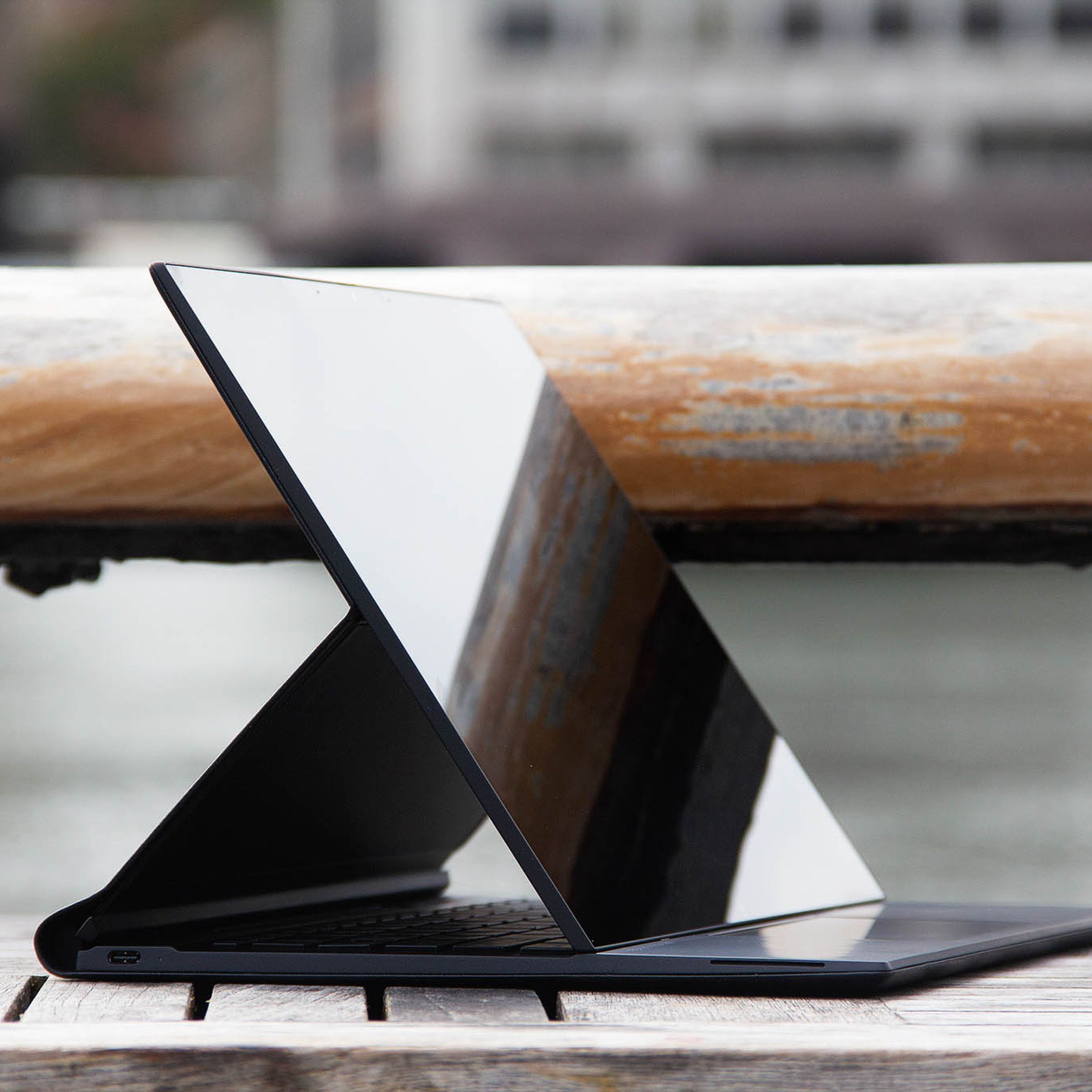 The HP Elite Folio in easel mode, angled to the right, on an outdoor table with a river in the background.