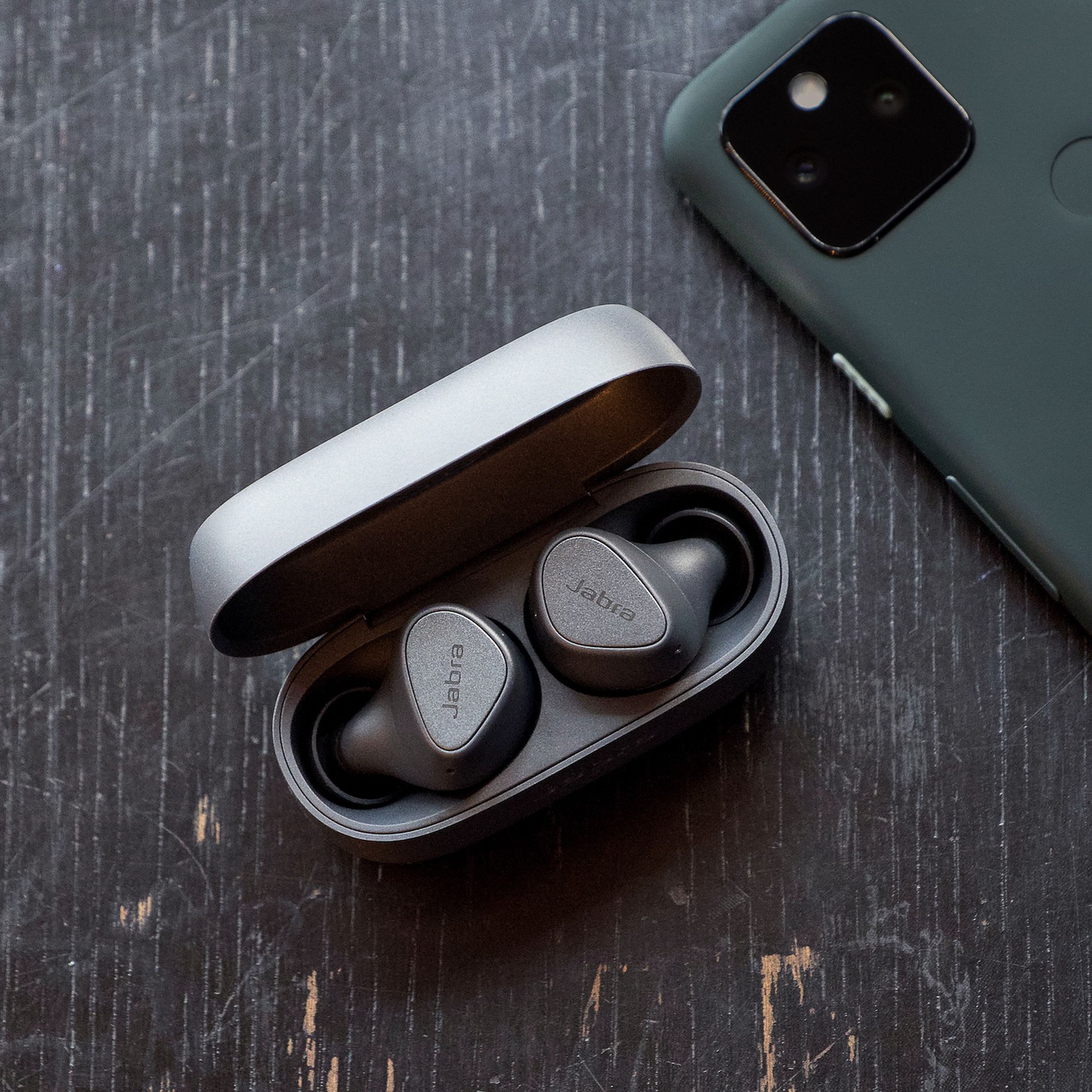 A pair of Jabra’s Elite 3 wireless earbuds sitting on a table near a phone.