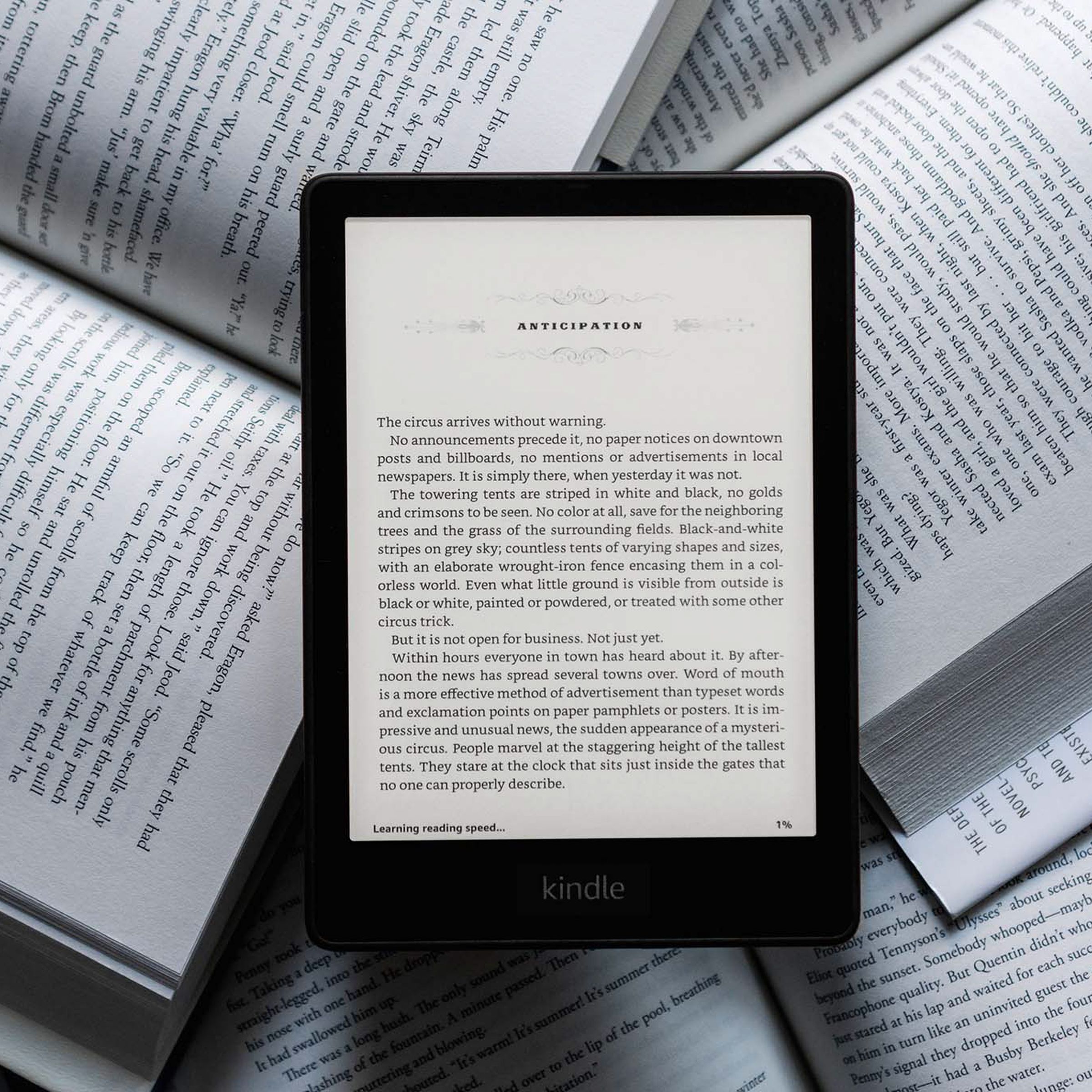 The Kindle Paperwhite lying on a bunch of physical books while turned on.