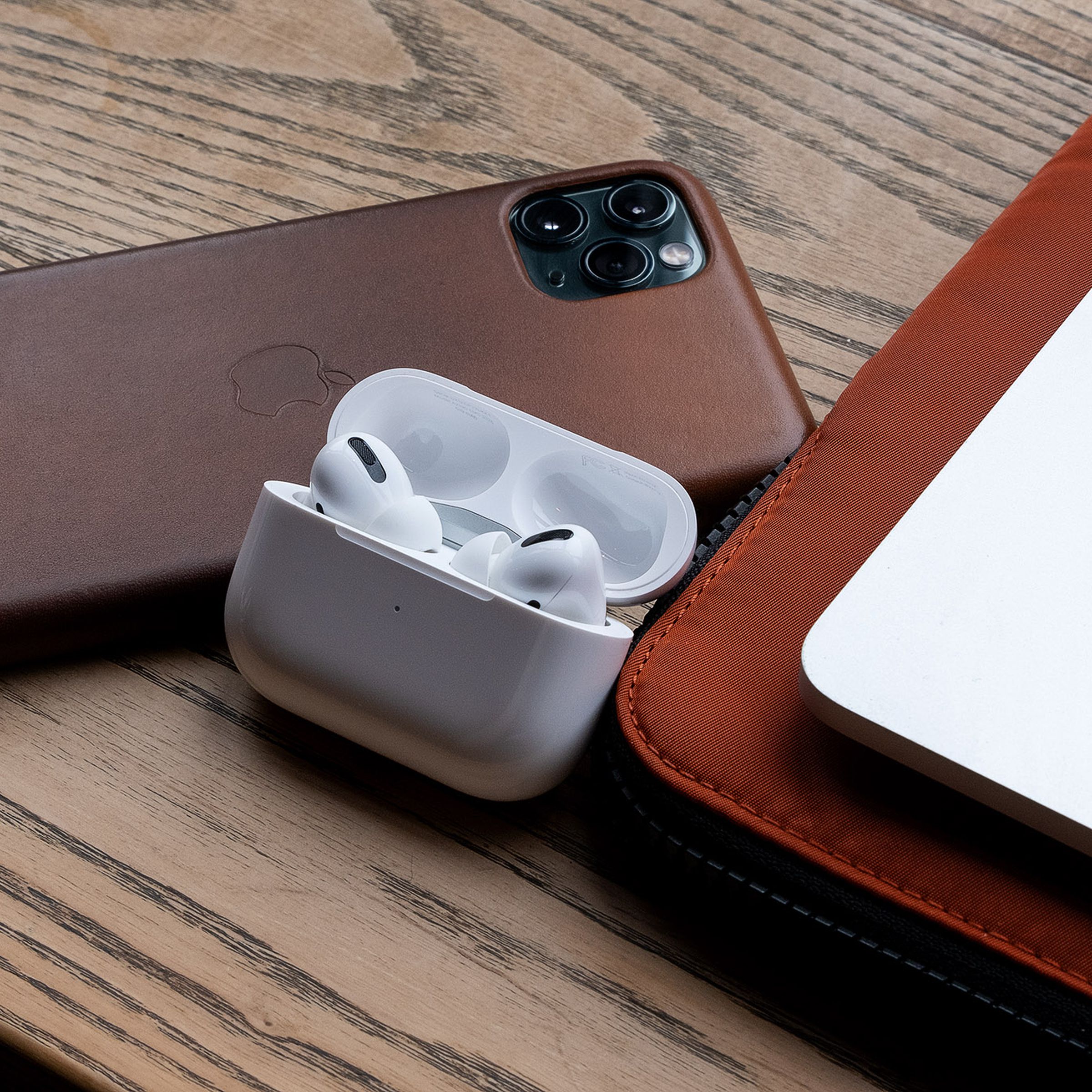 First-generation AirPods Pro lying on a desk near a laptop and an iPhone.