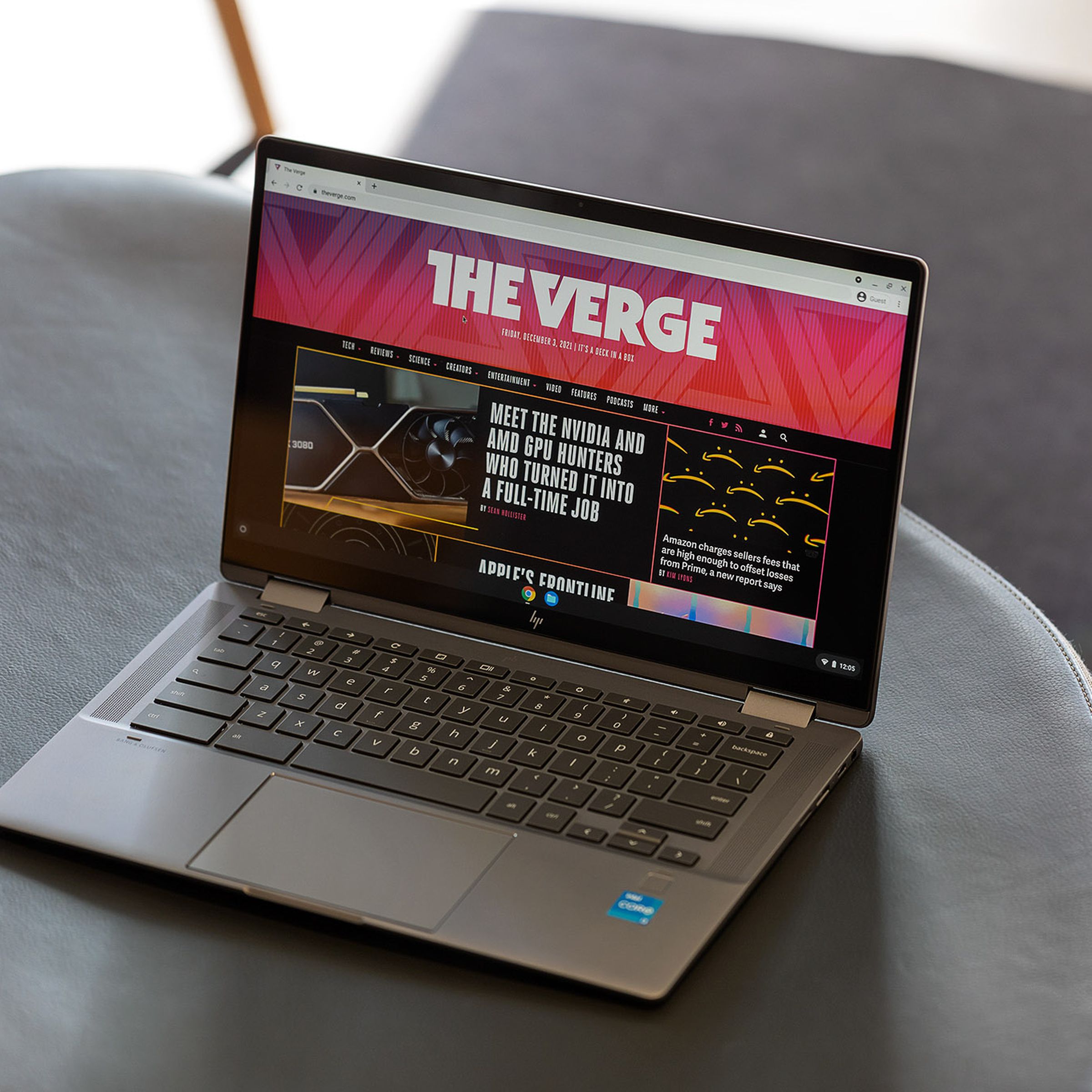 The HP Chromebook x360 14c open on a gray bench seen from above and to the right. The screen displays The Verge homepage.