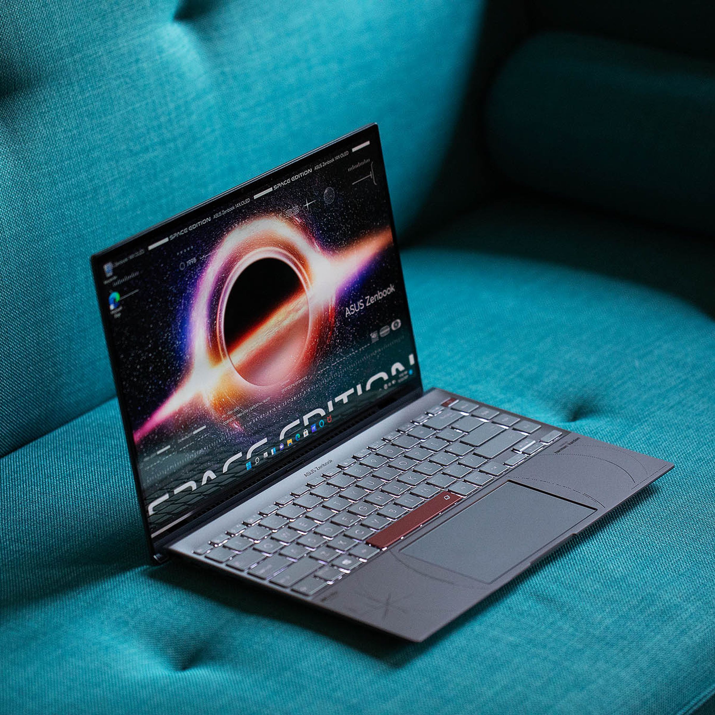 The Asus Zenbook 14 OLED Space Edition on a green couch angled to the right, open, from above. The screen displays a supernova with the words Space Edition across the bottom.