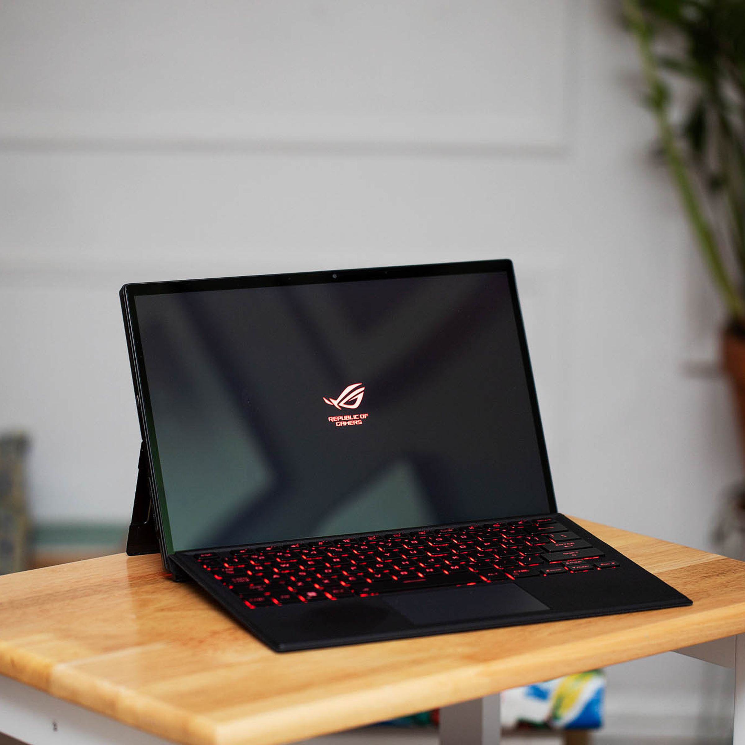 The Asus ROG Flow Z13 in laptop mode on a small table. The screen displays the ROG logo.