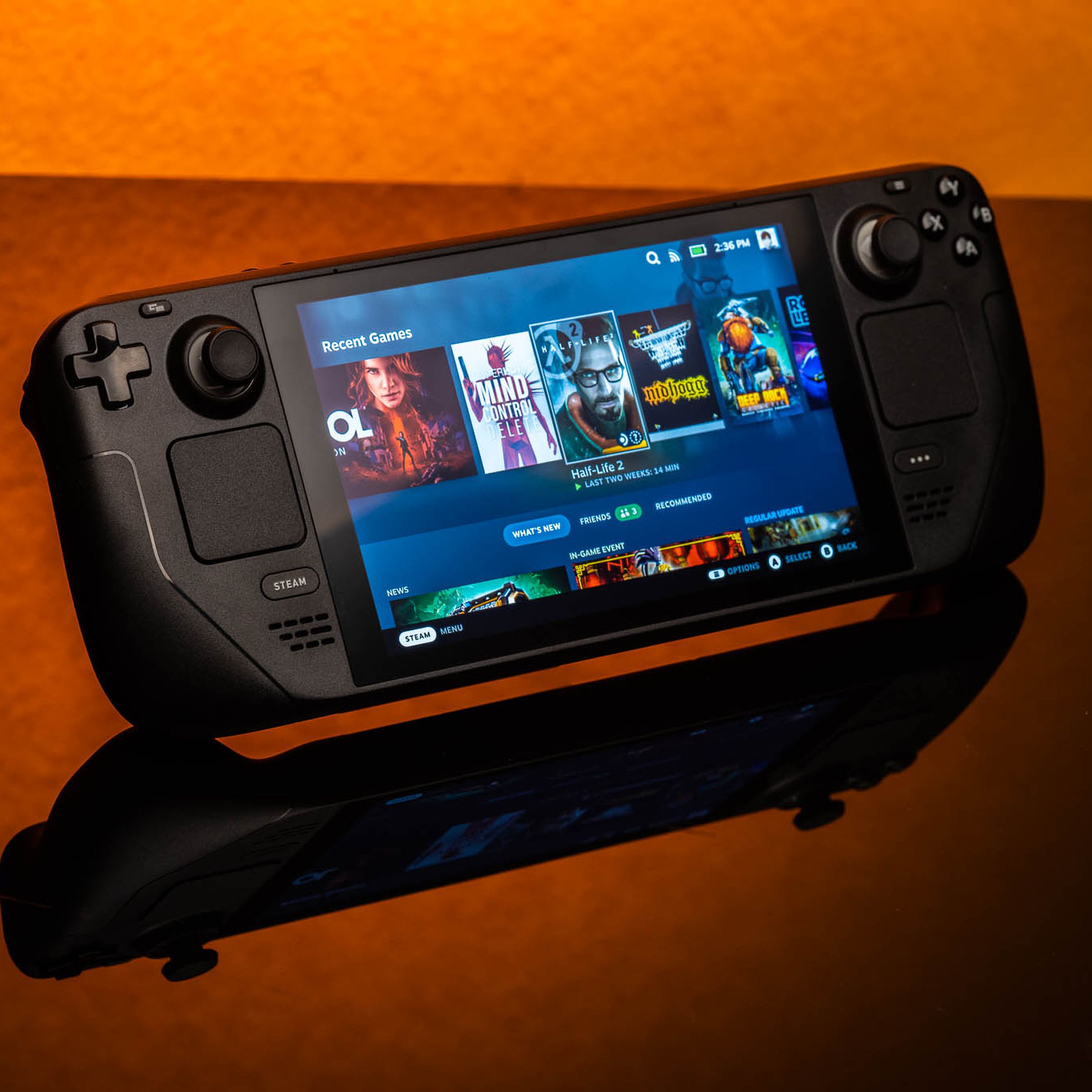 The Valve Steam Deck gaming handheld sits on a reflective table, with an orange background.
