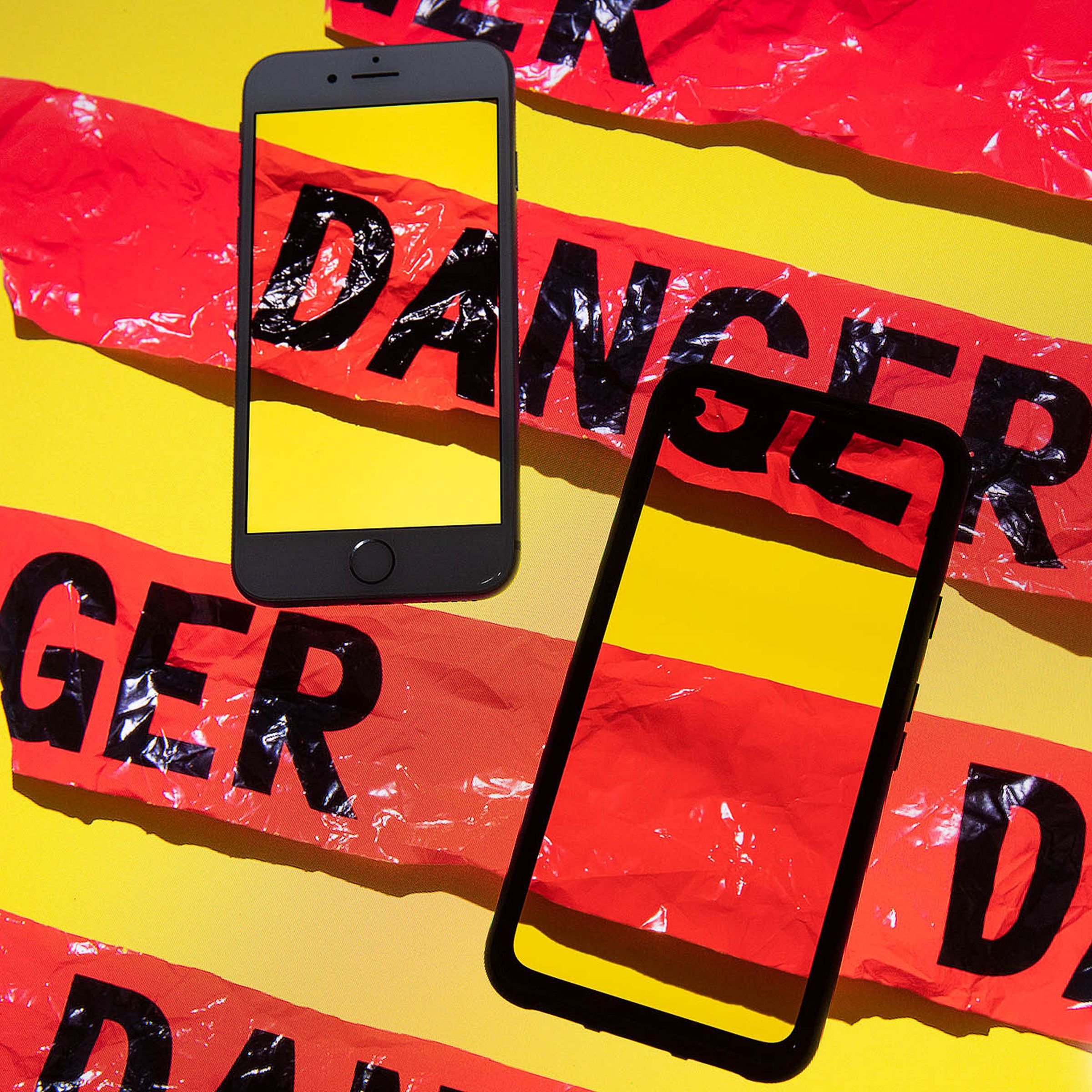 Illustration of two smartphones sitting on a yellow background with red tape across them that reads “DANGER”