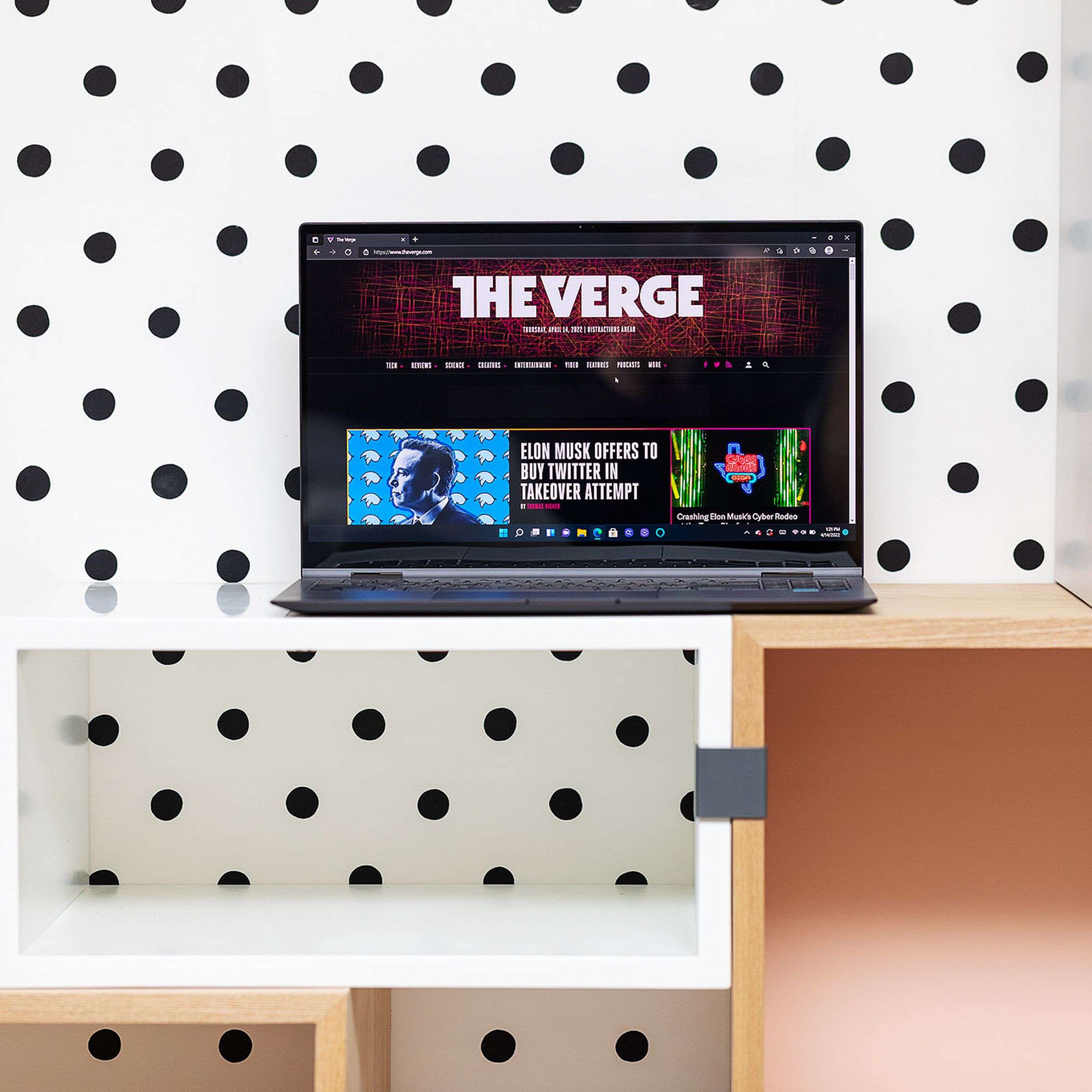 The Samsung Galaxy Book2 Pro 360 in front of polka dot wallpaper. The screen displays The Verge homepage.