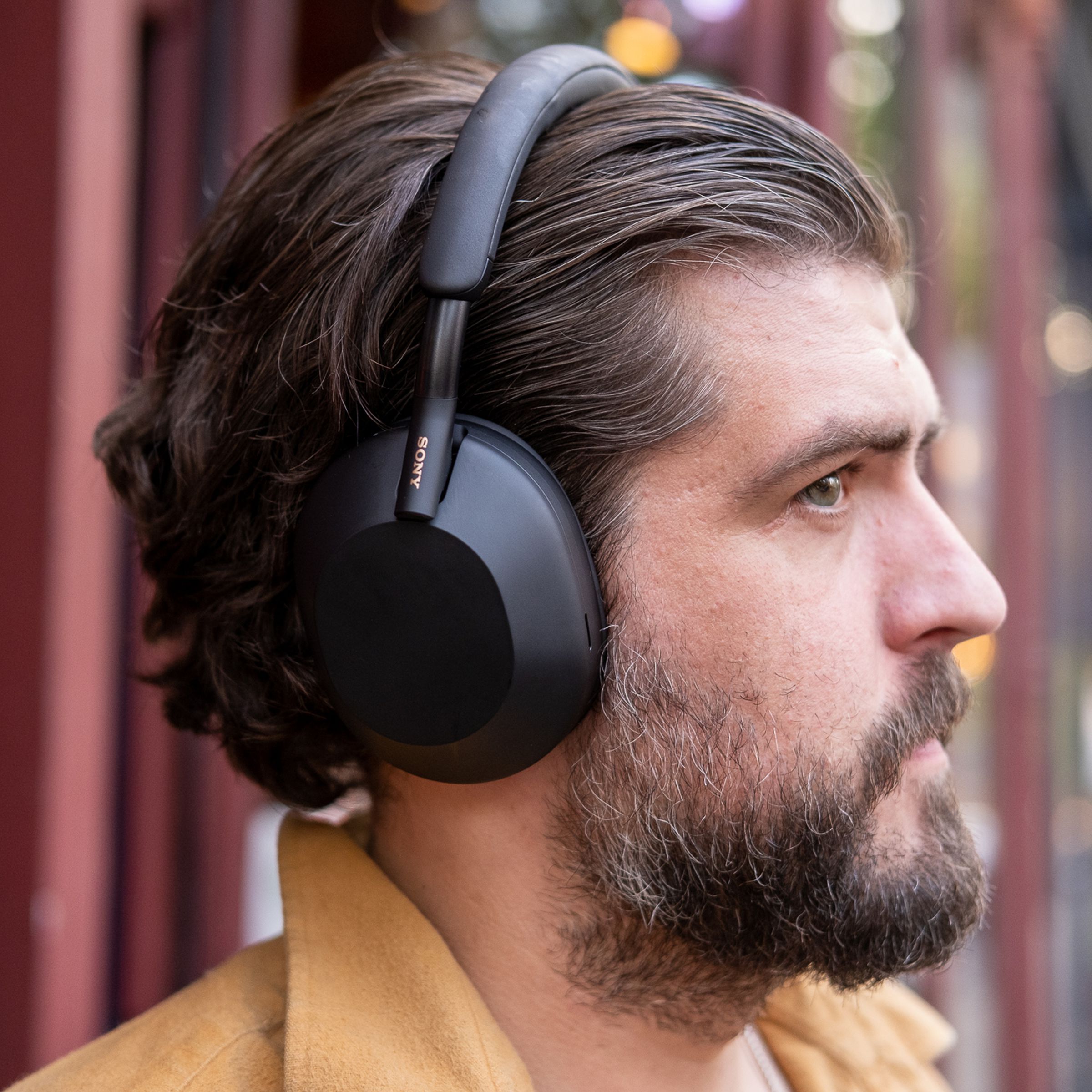 A man wearing Sony’s black WH-1000XM5 noise-canceling headphones outside.