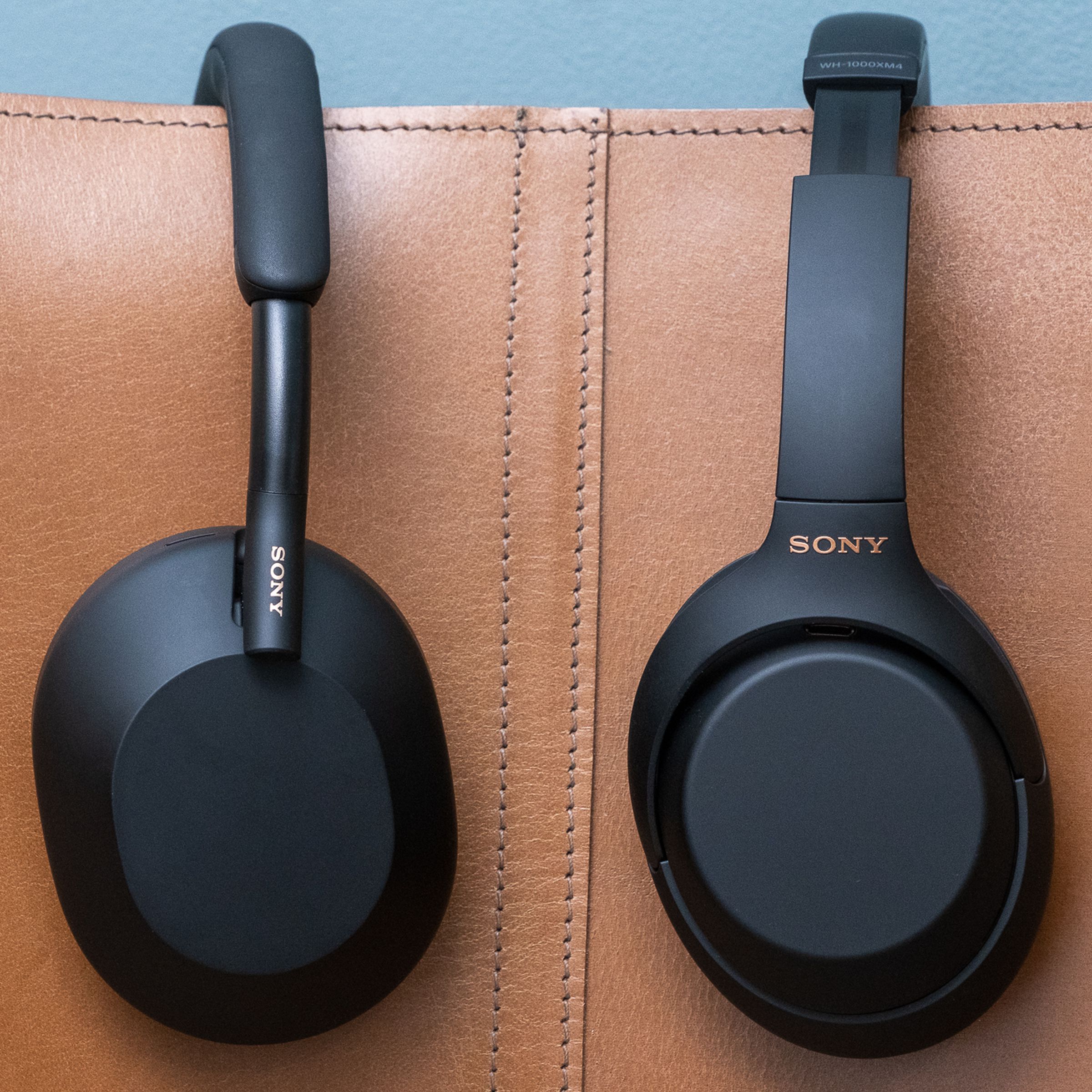 The Sony’s WH-1000XM5 (left) and last-gen WH-1000XM4 (right) hanging on a couch.