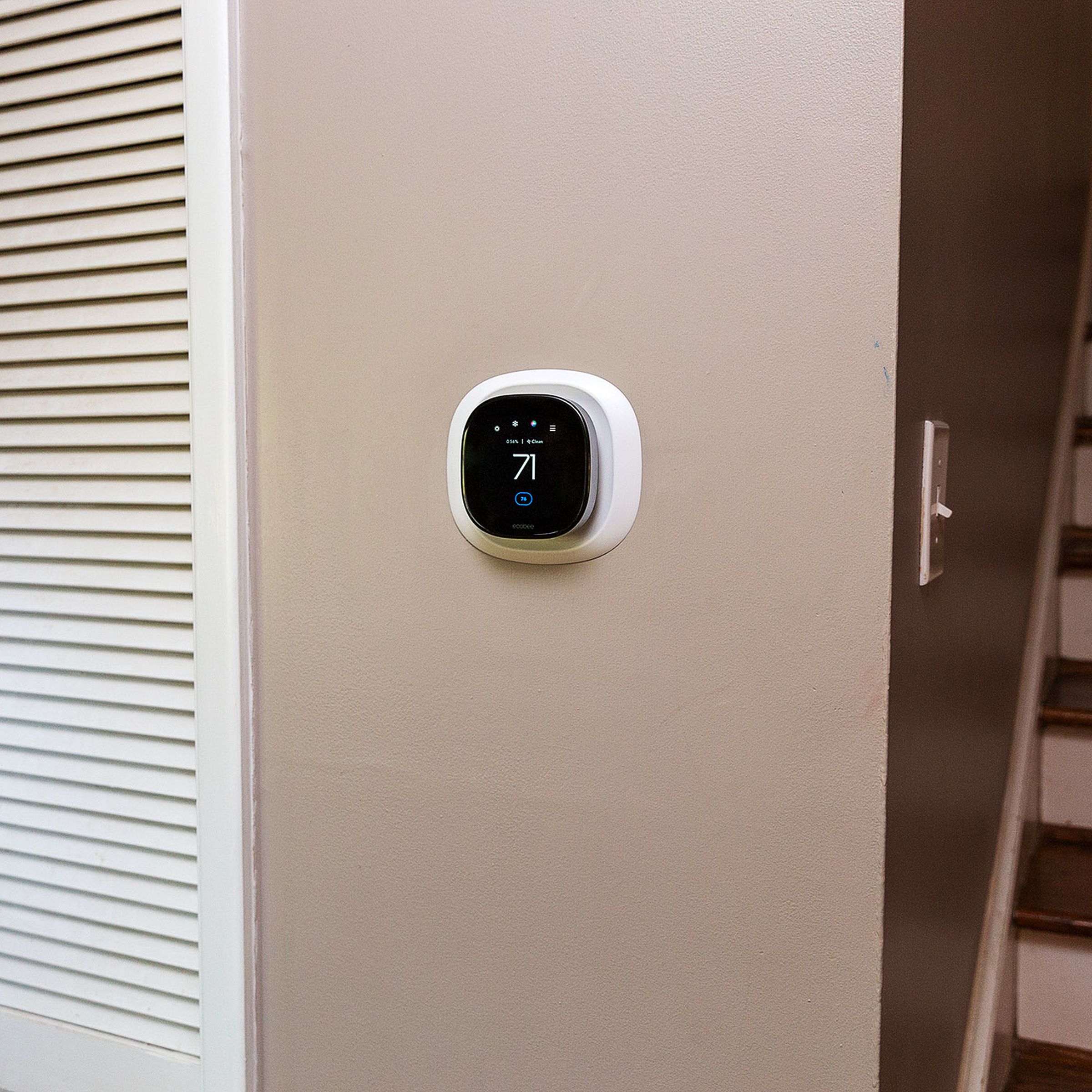 Small Ecobee thermostat on a tan wall in between closet and staircase.