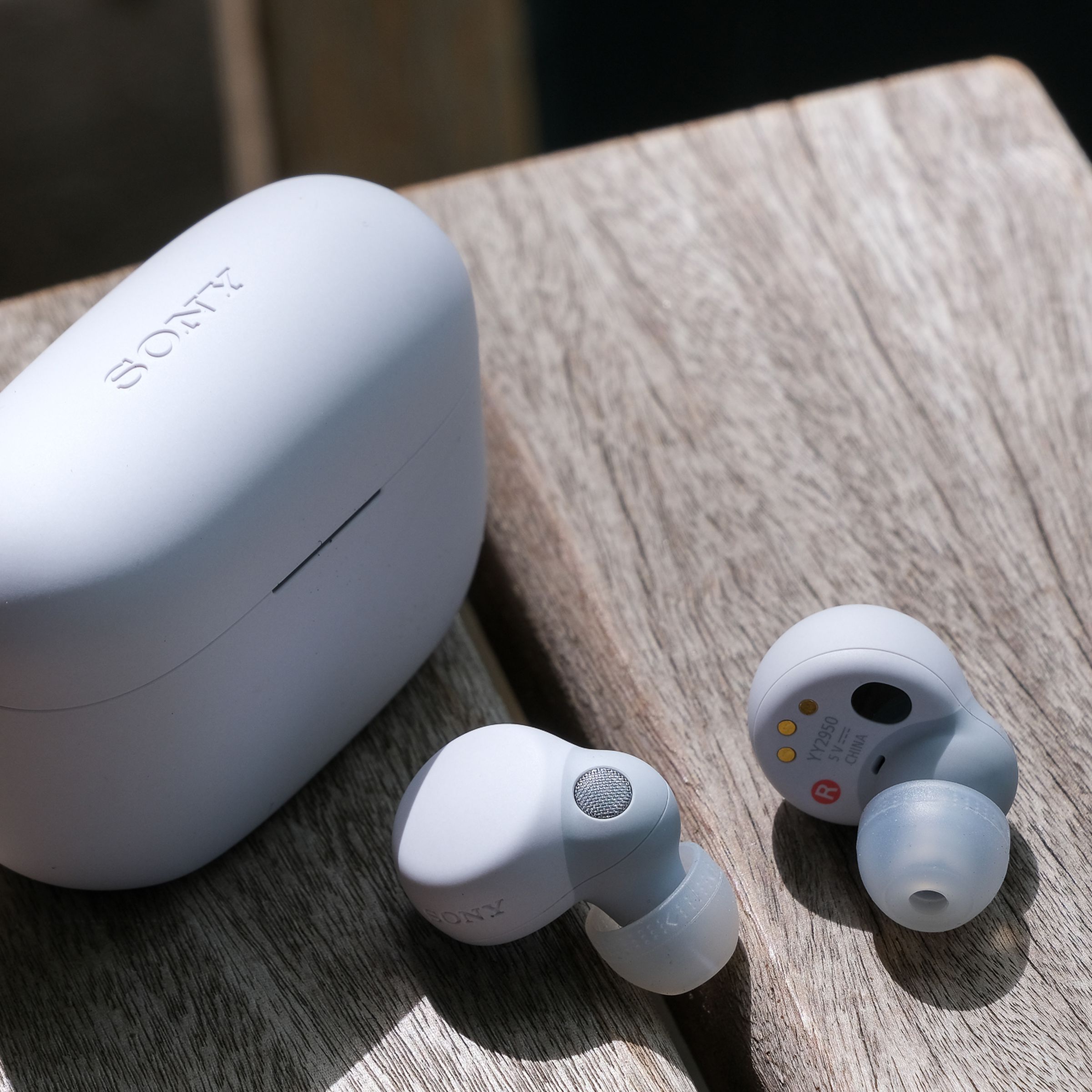 The white Sony LinkBuds S wireless earbuds and their charging case sitting on the edge of a wood table.