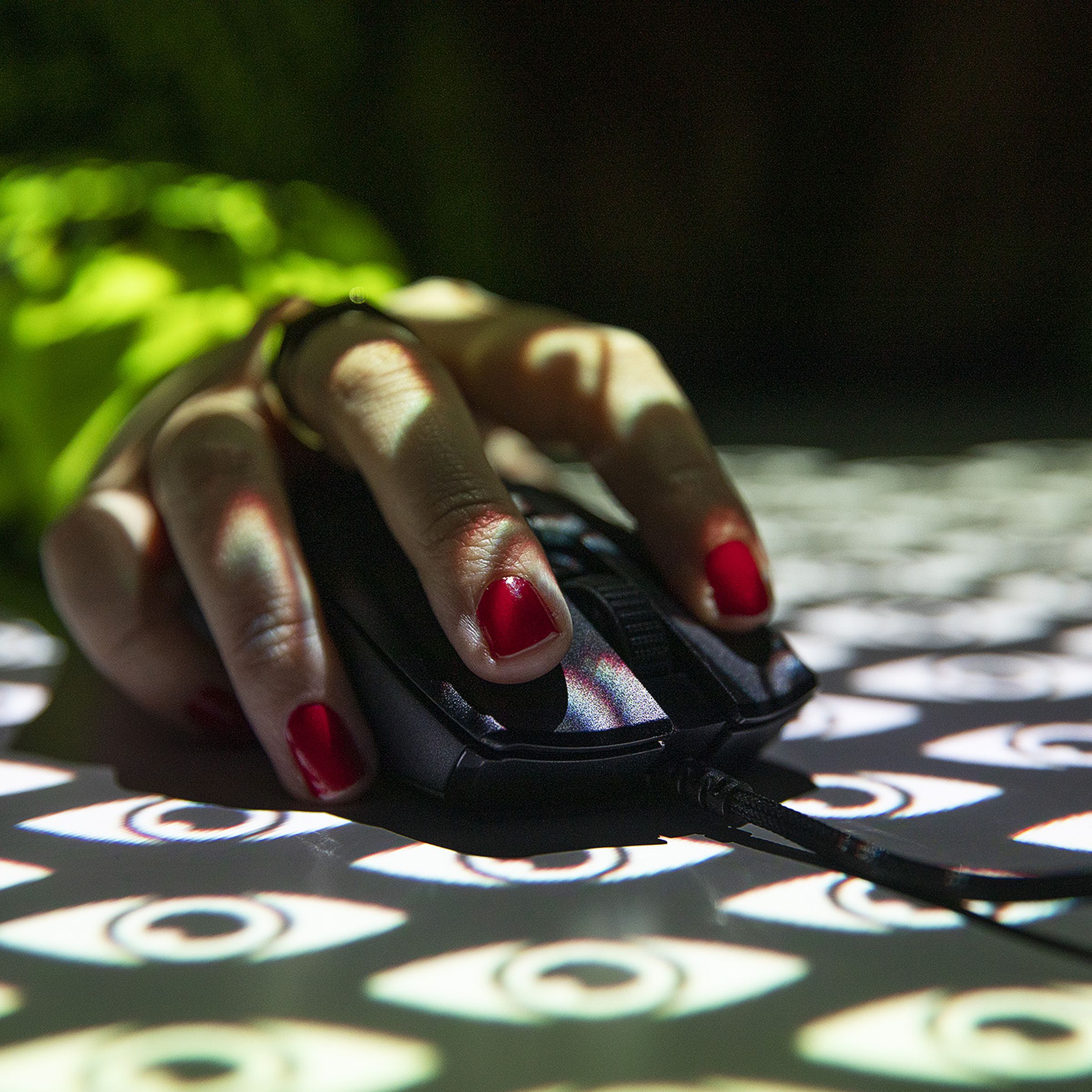 Photograph of a hand wearing red nail varnish holding a mouse with a projection overlay of stylized eyes