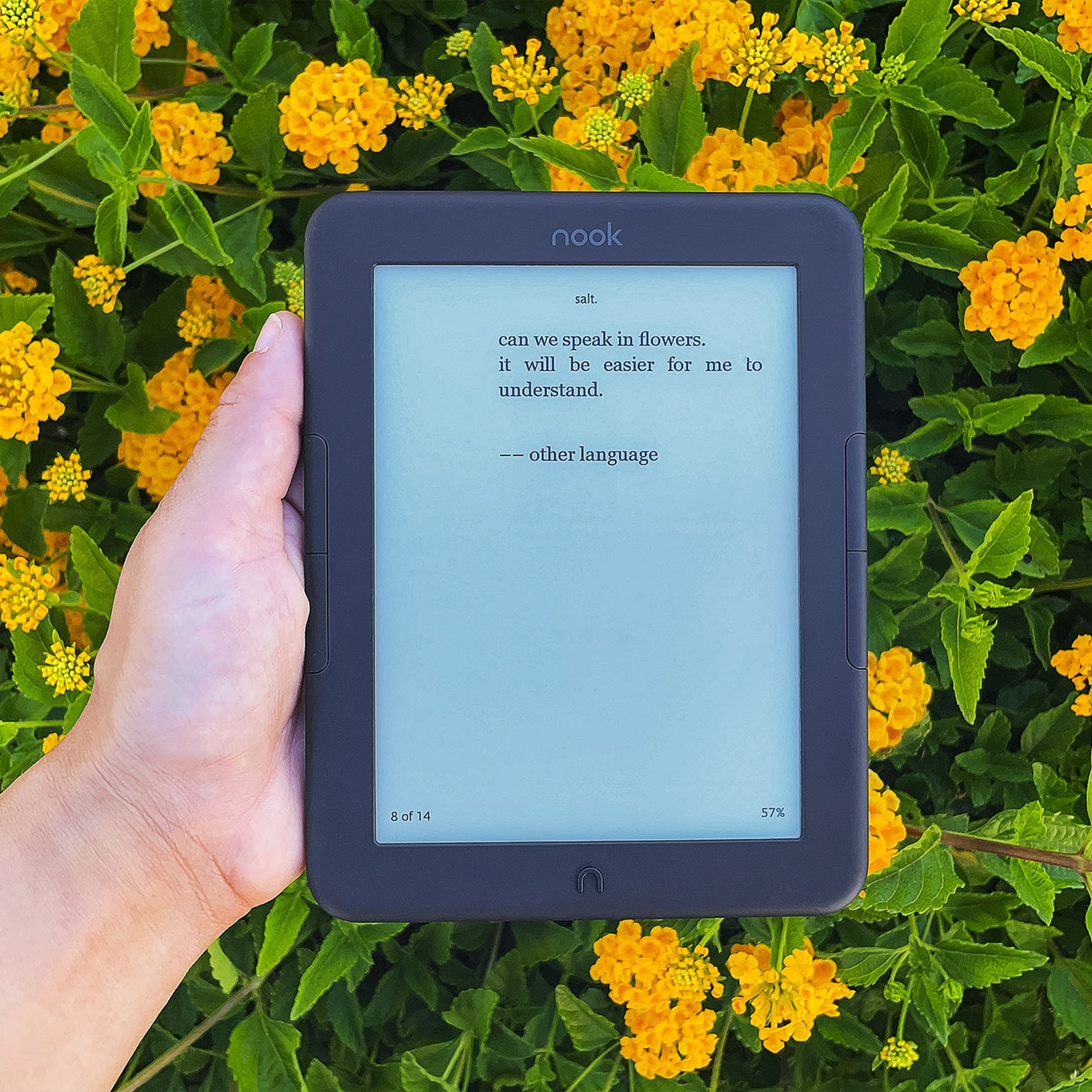 An image of an e-reader being held in front of yellow flowers.