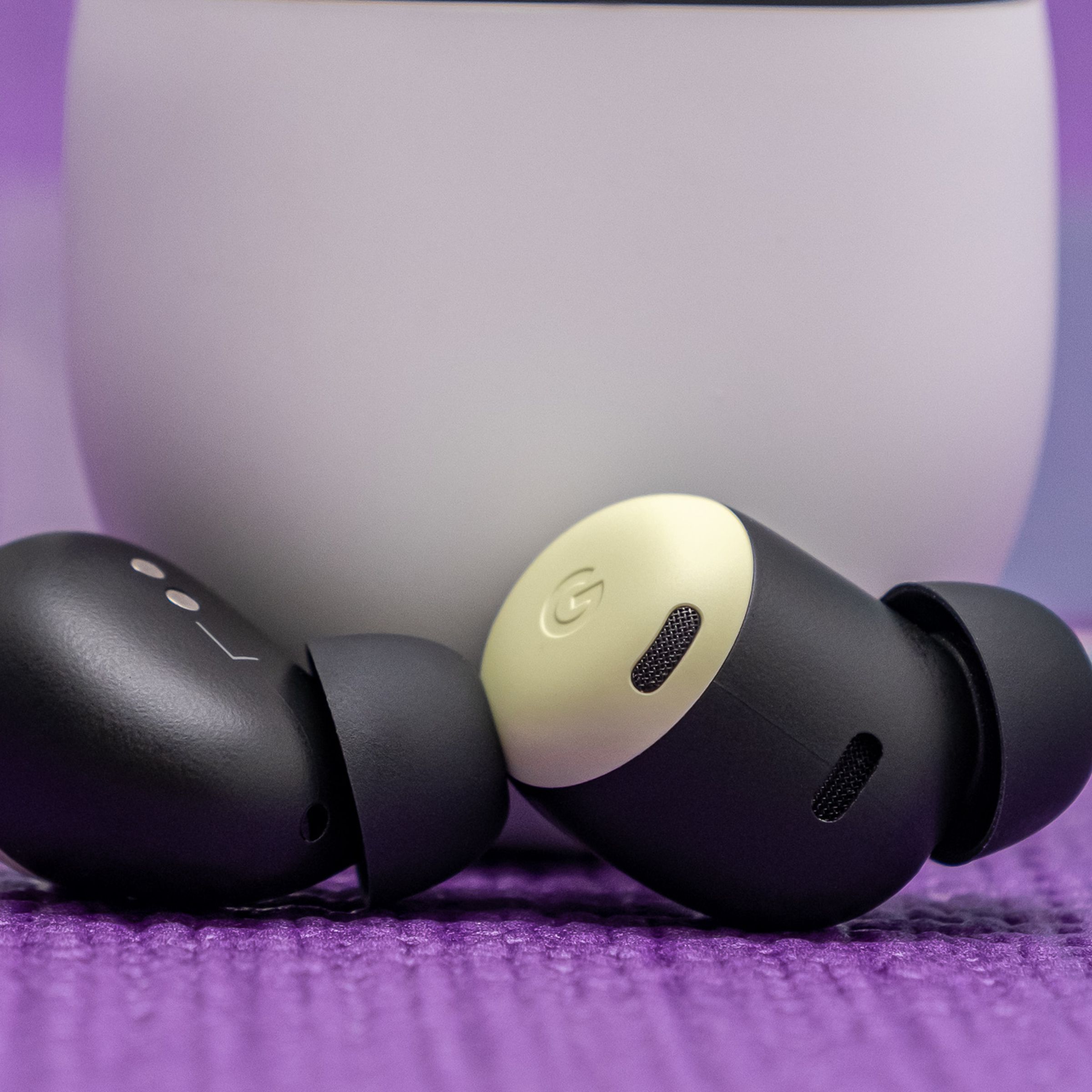 Google’s Pixel Buds Pro earbuds, in yellow lemongrass color, resting at the foot of their white charging case on a tabletop.