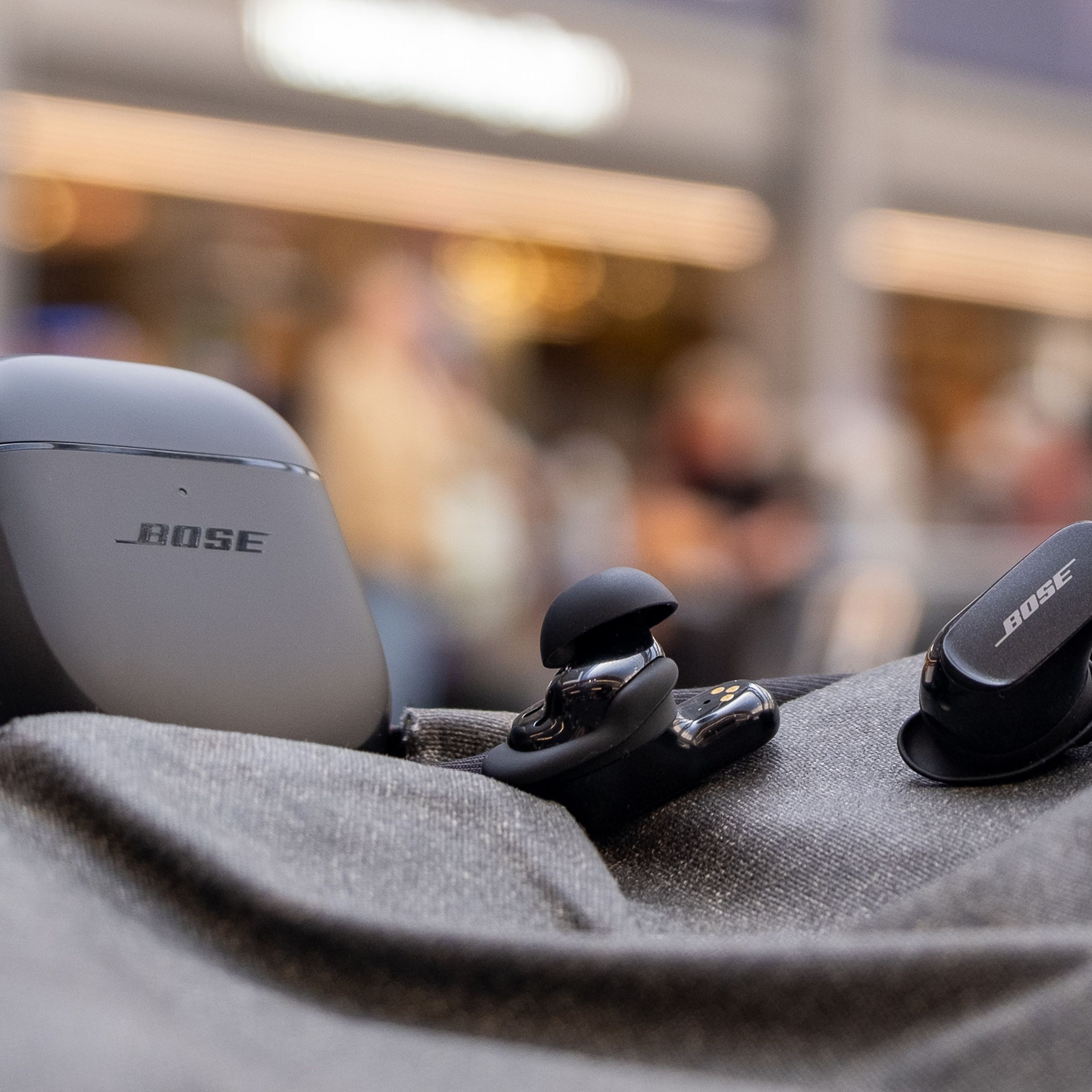 An image of the Bose QC Earbuds II on top of a backpack in a train terminal.