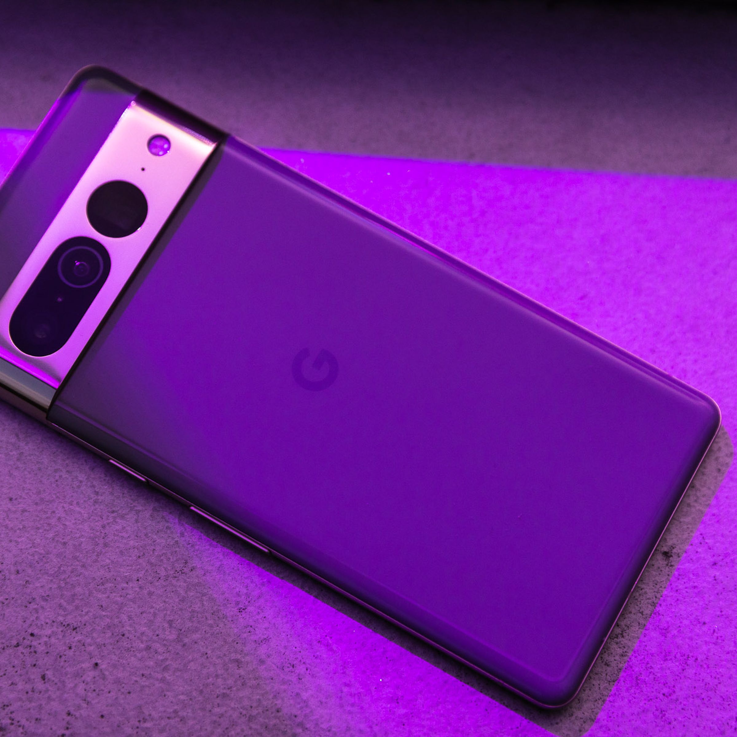 A Pixel 7 Pro with a glossy gold visor lays on its front on a table and a purple light is aimed at it.
