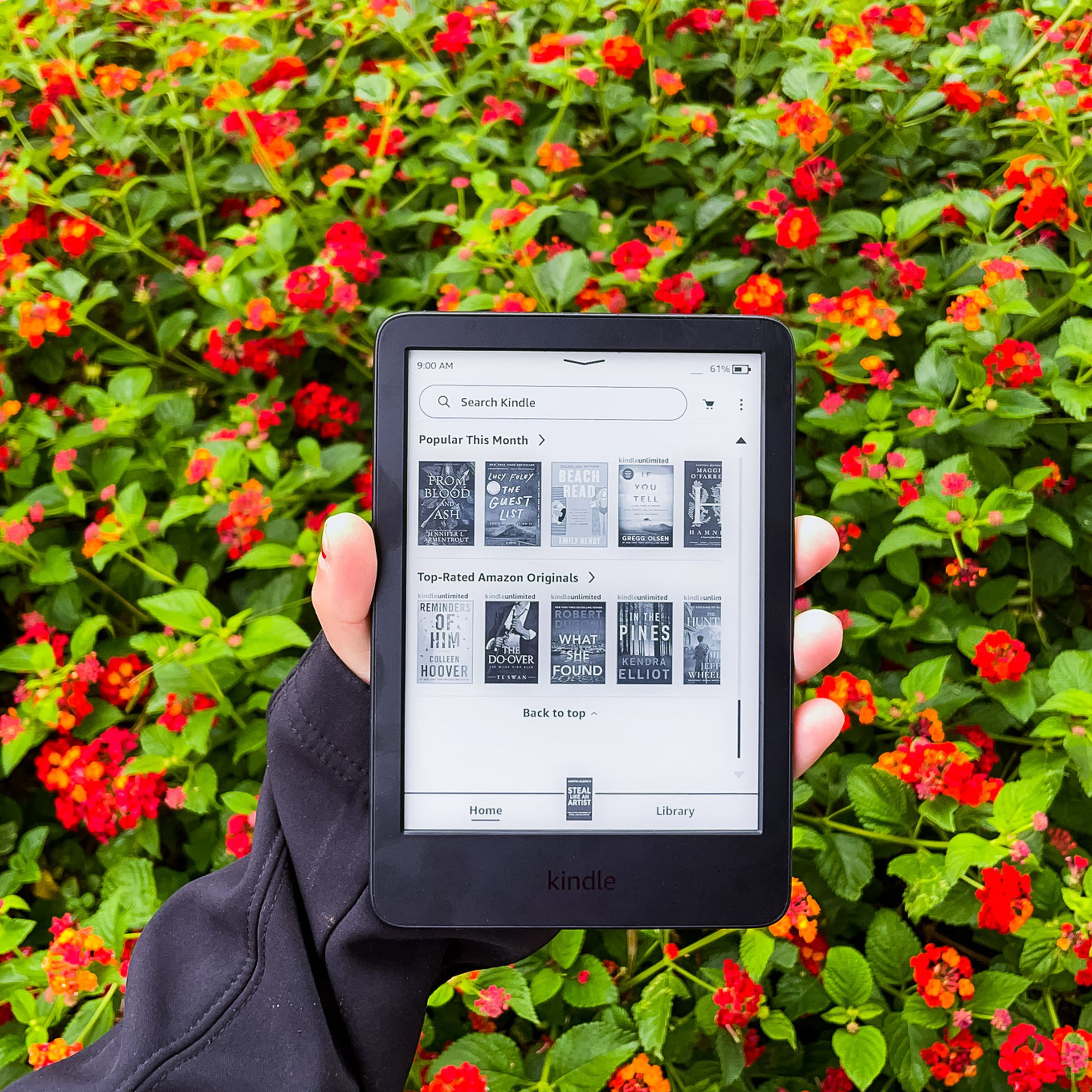 A hand holding the Kindle and displaying the main menu of the device.