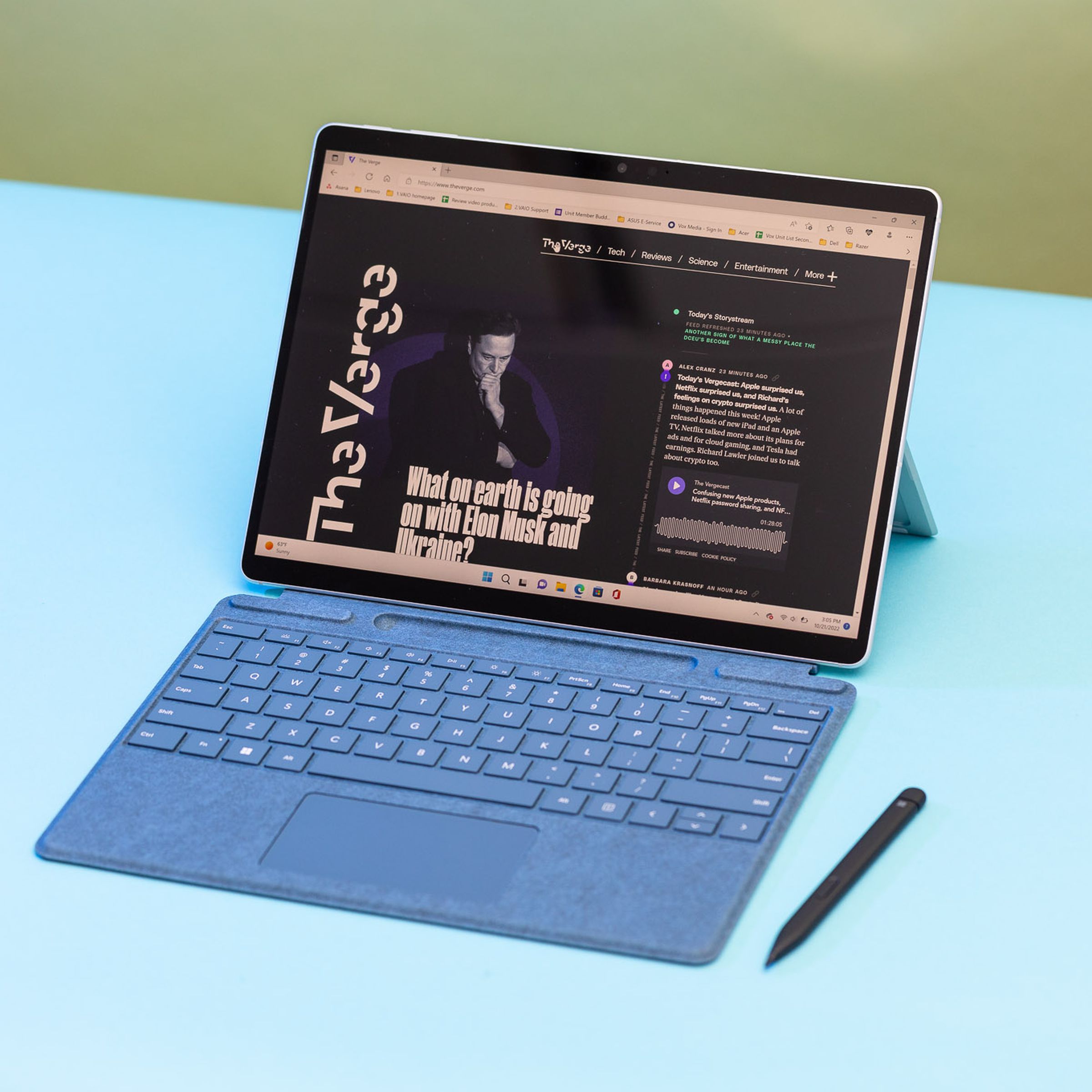The Surface Pro 9 in laptop mode seen from above with the stylus beside it. The screen displays The Verge homepage.