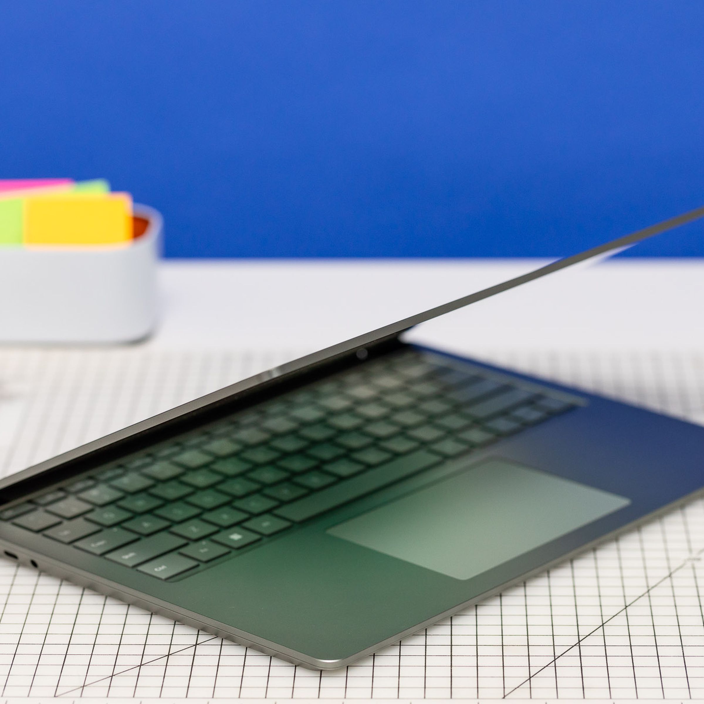 The Surface Laptop 5 half open on a gridded table with post-it notes in the background.