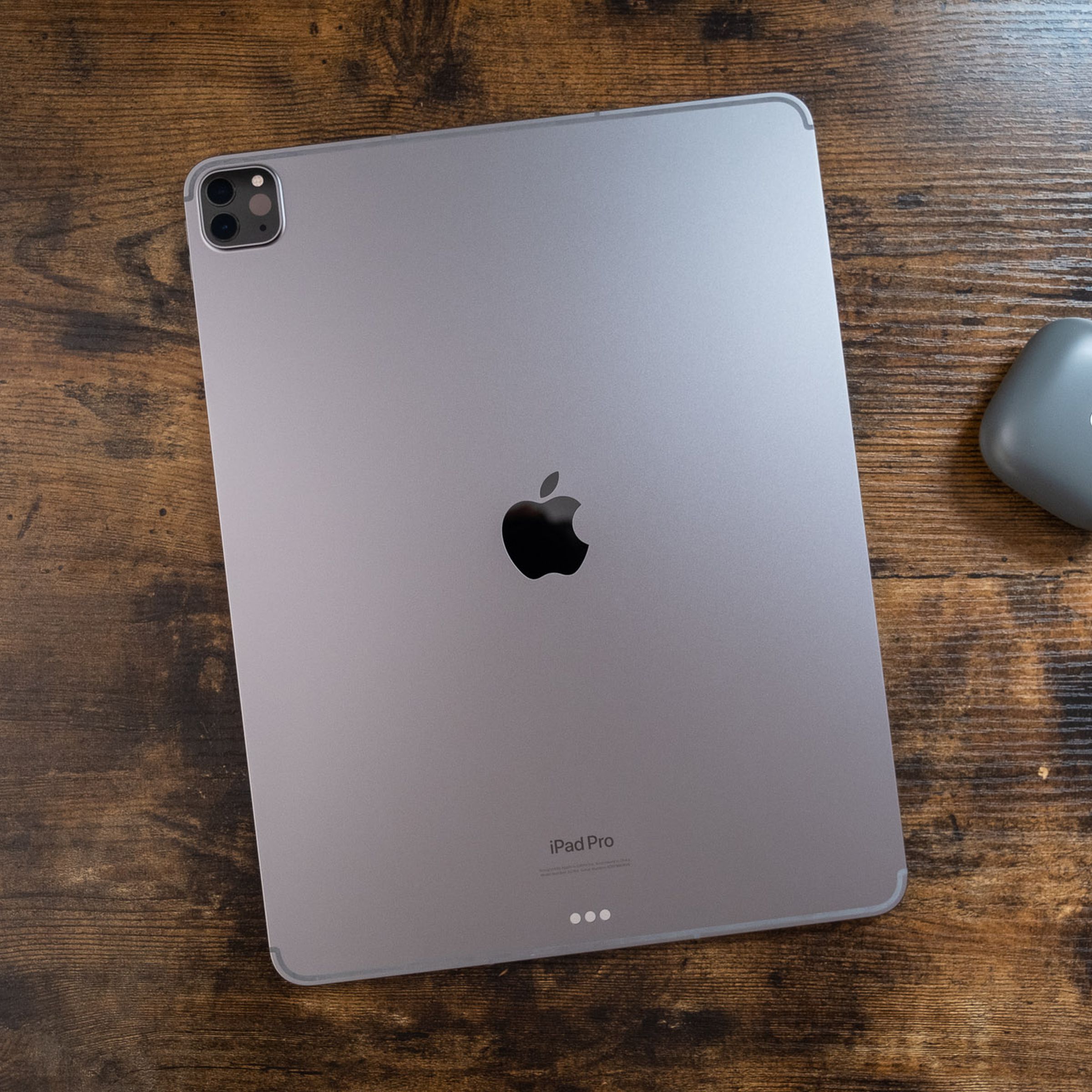 Un iPad Pro gris espacial de 12,9 pulgadas colocado boca abajo sobre una mesa de madera, visto desde arriba hacia abajo.