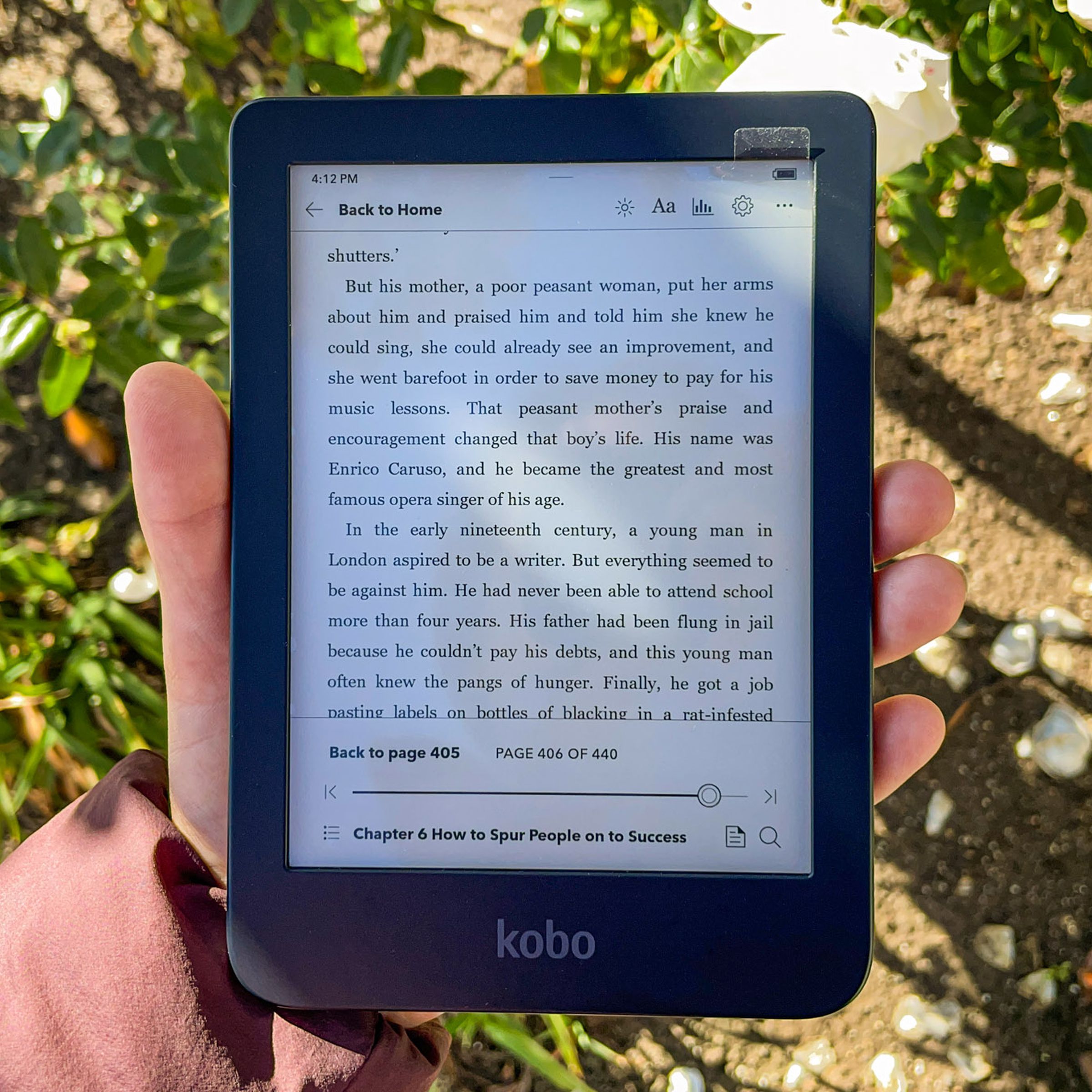 Image of a hand holding up the Kobo Clara 2E. Its display is on and open to a page in an ebook.