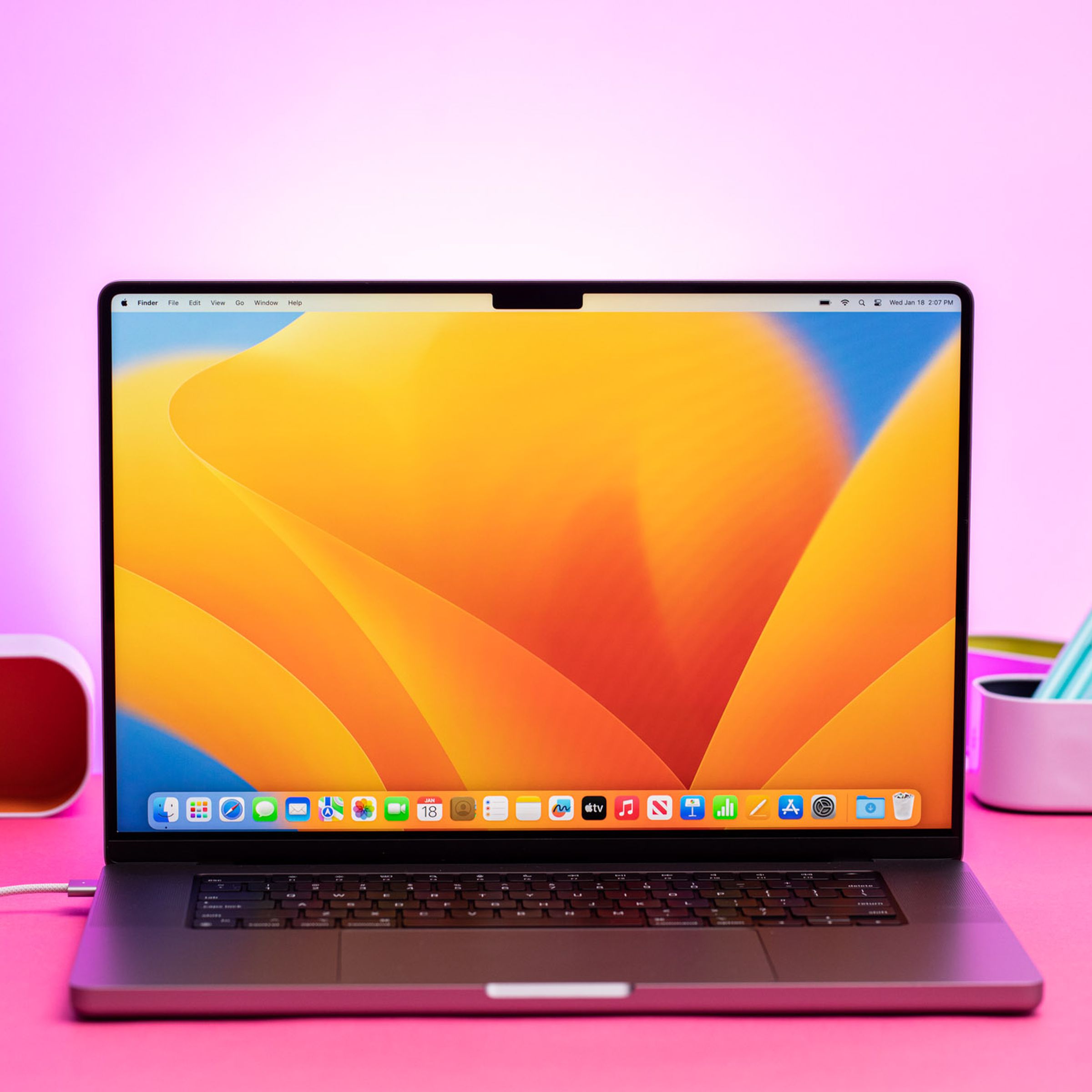 جهاز MacBook Pro 16 (2023) على طاولة وردية. تعرض الشاشة نمط سطح المكتب باللونين الأزرق والأصفر.