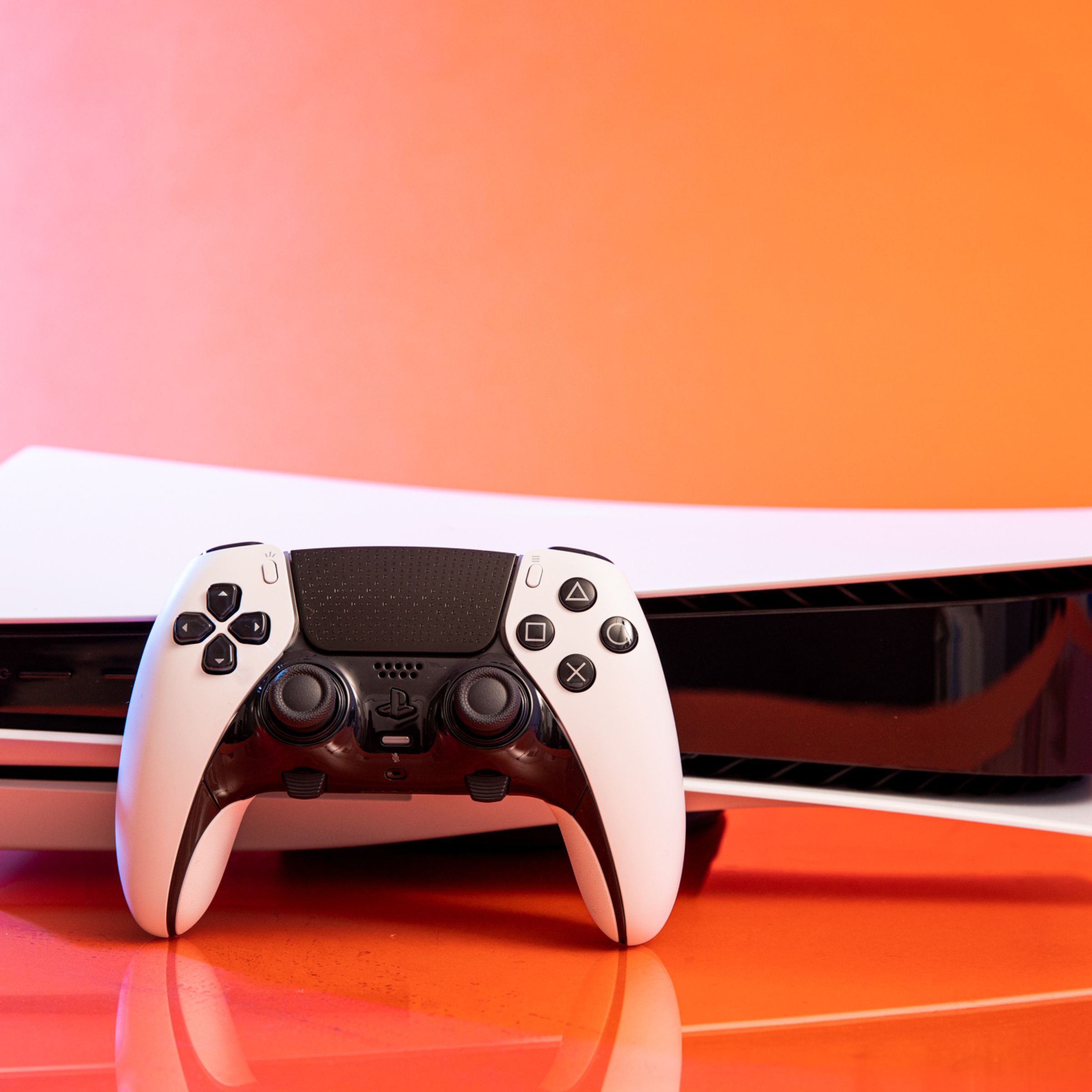 A Sony DualSense Edge controller resting on a PlayStation 5 with an orange background.