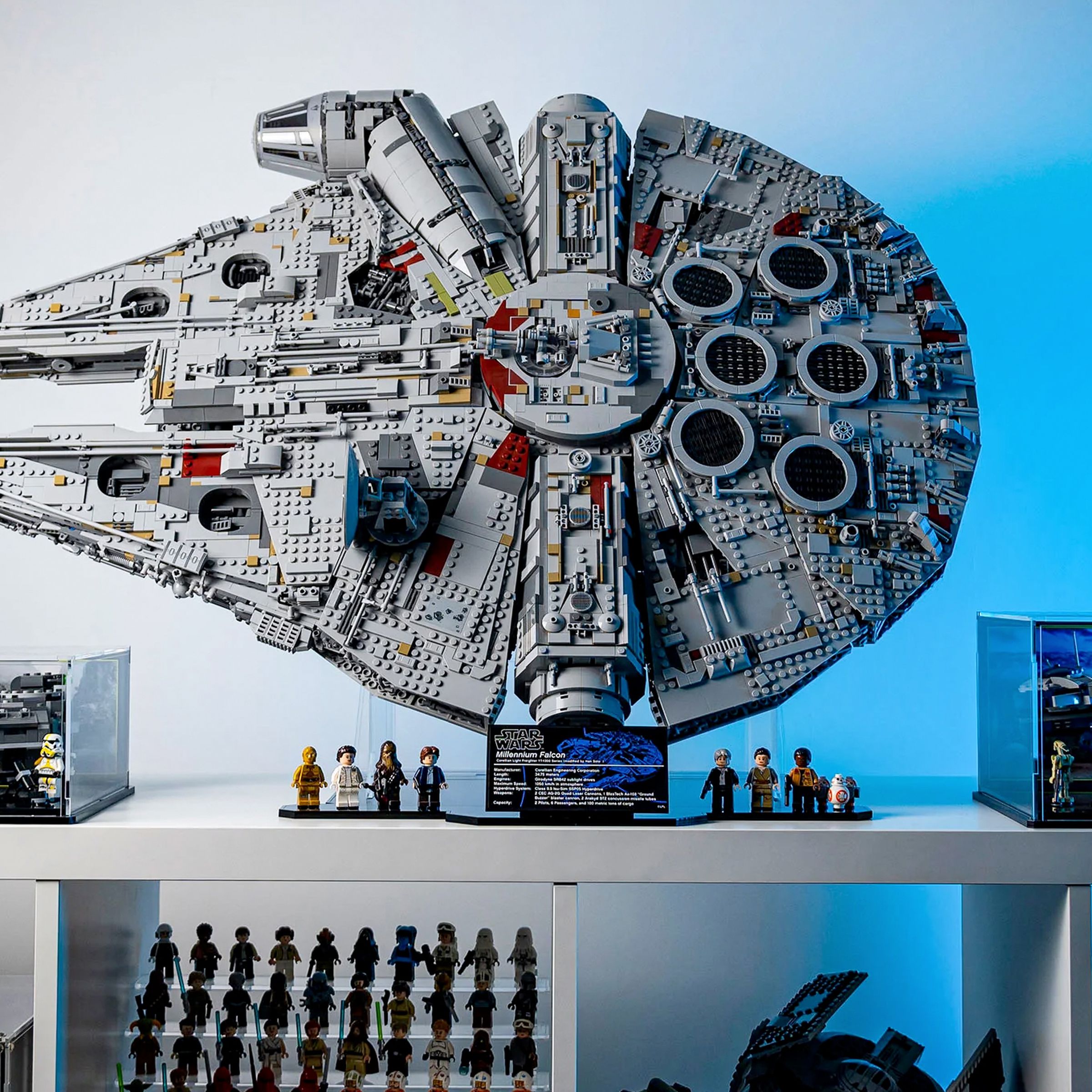A built Lego Star Wars Millennium Falcon set mounted on a vertical stand from Wicked Brick, sitting atop a white shelf with other Star Wars collectibles.