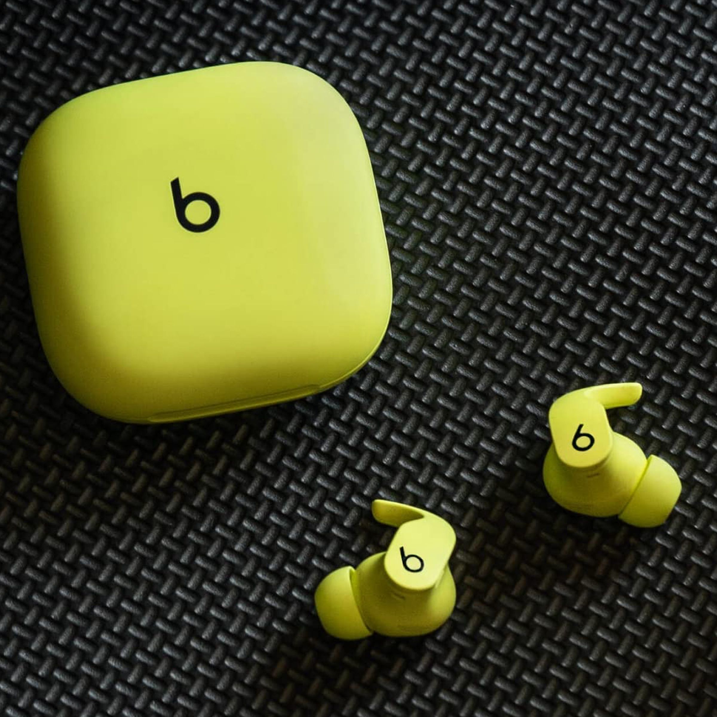 The bright yellow version of the Beats Fit Pro earbuds and their matching case resting on a black mesh pattern.