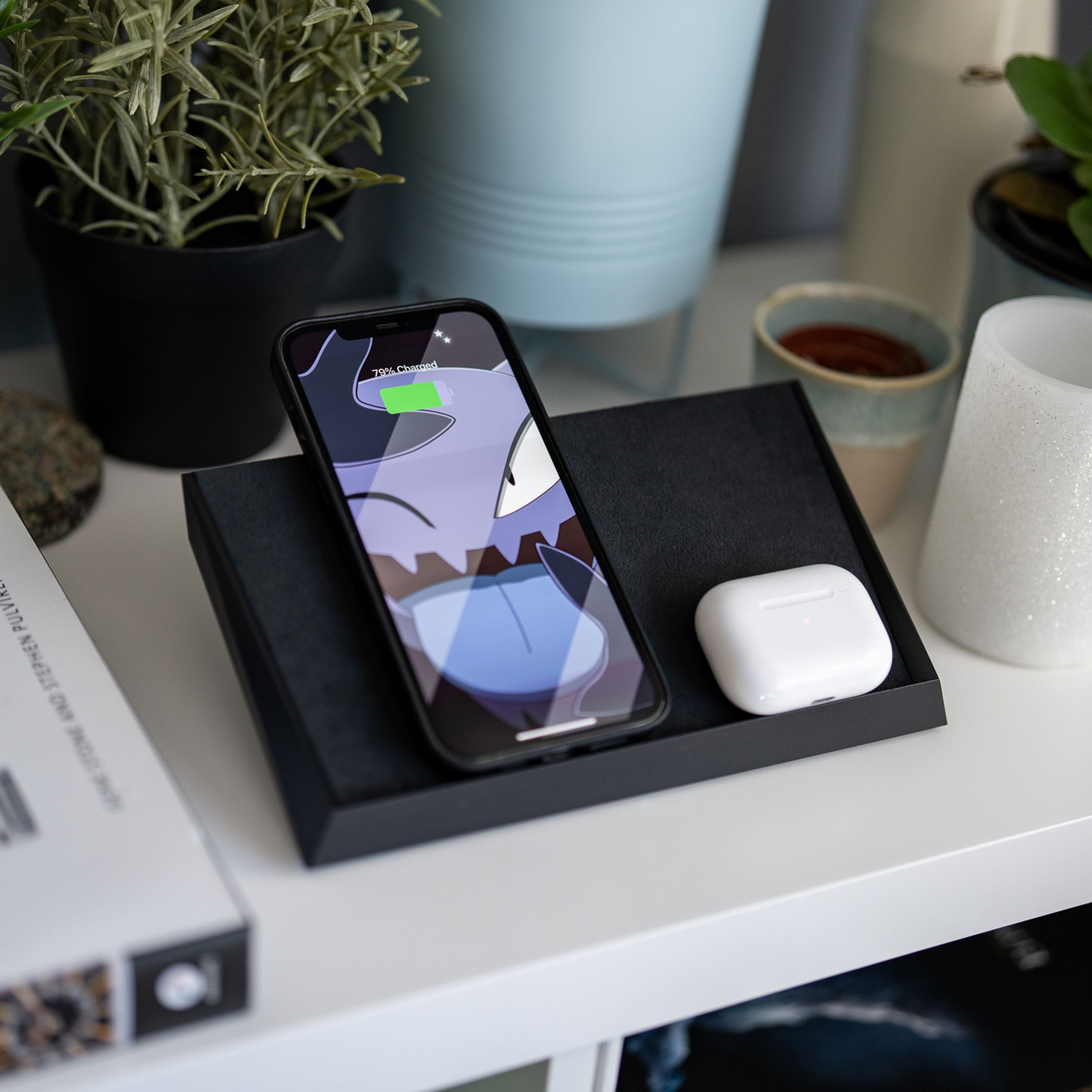 An iPhone and AirPods Pro case charging on Tesla’s wireless charging mat, sitting on a white end table.
