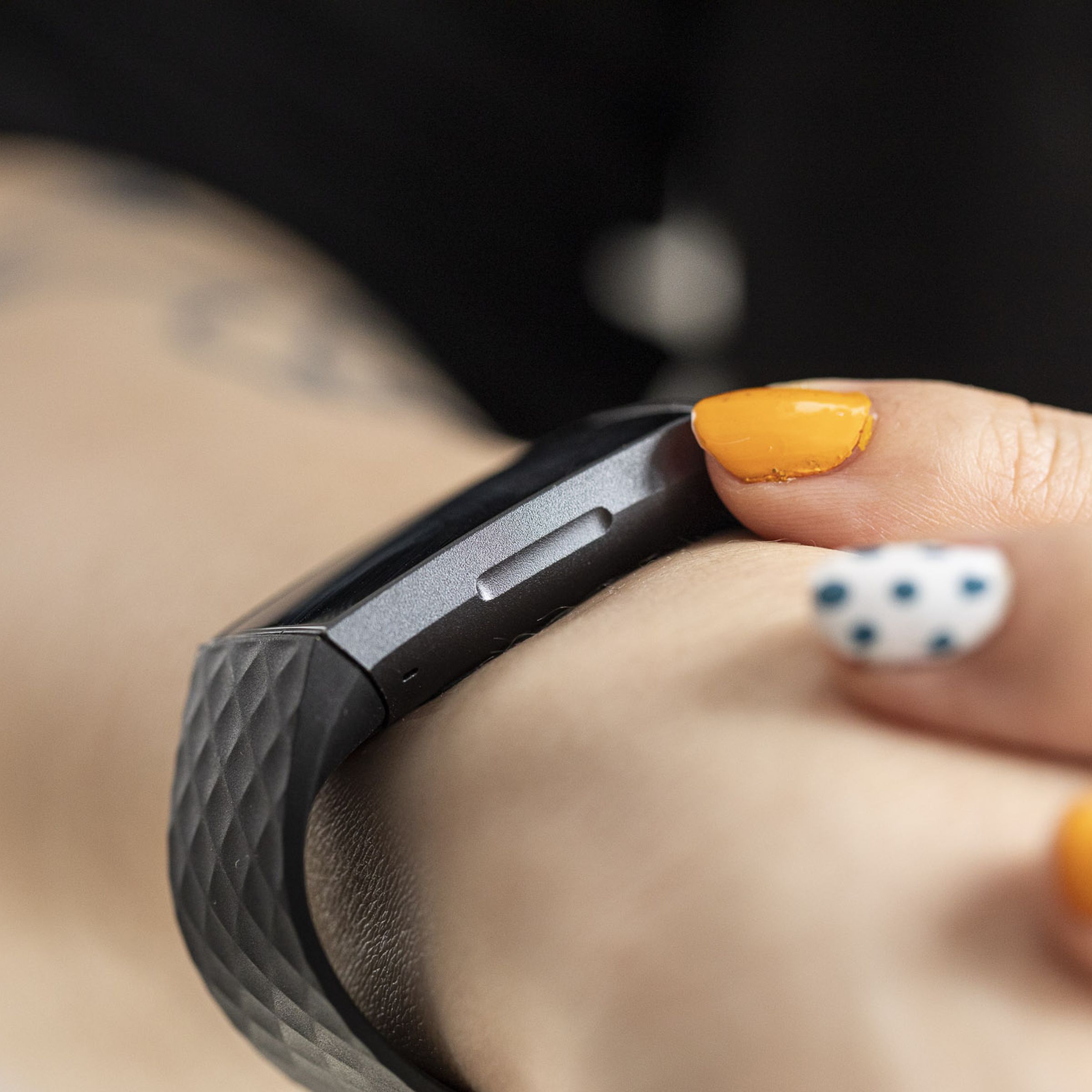 Person with colorful manicure using the Fitbit Charge 3 with a clear view of the inductive button.