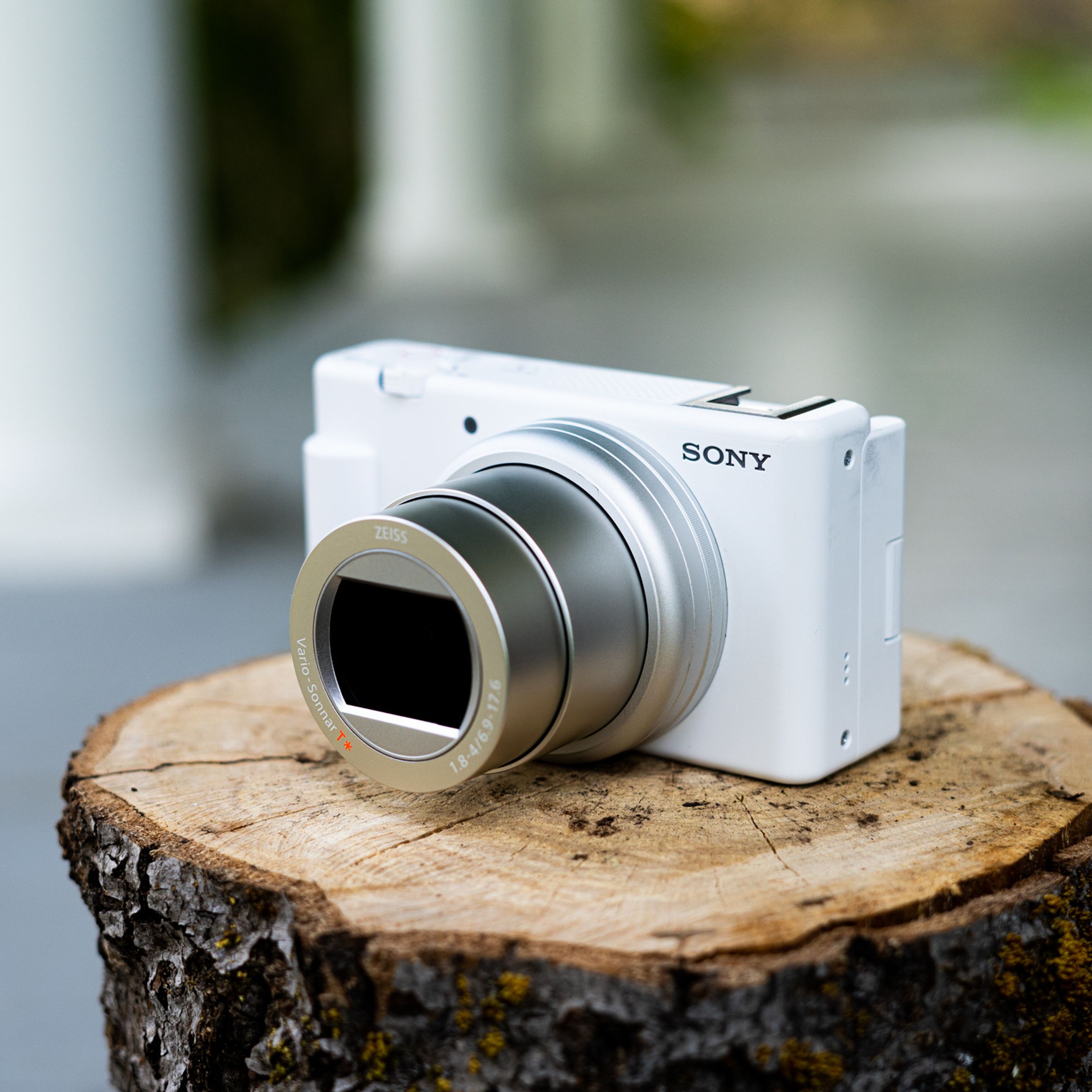 The Sony ZV-1 II camera, in white and silver, sitting on a cut log with its lens extended.