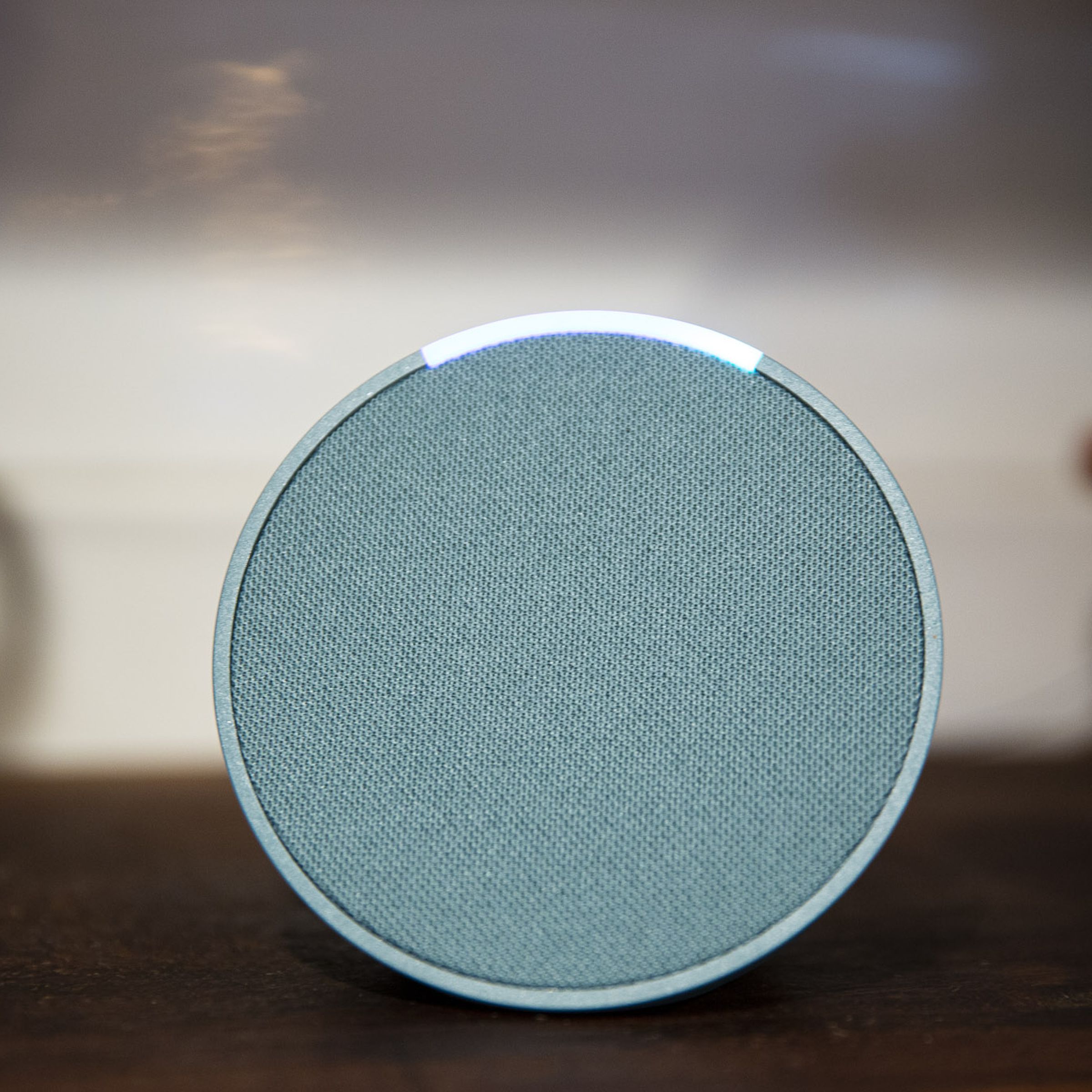 A green Echo Pop smart speaker on a countertop with its light on.