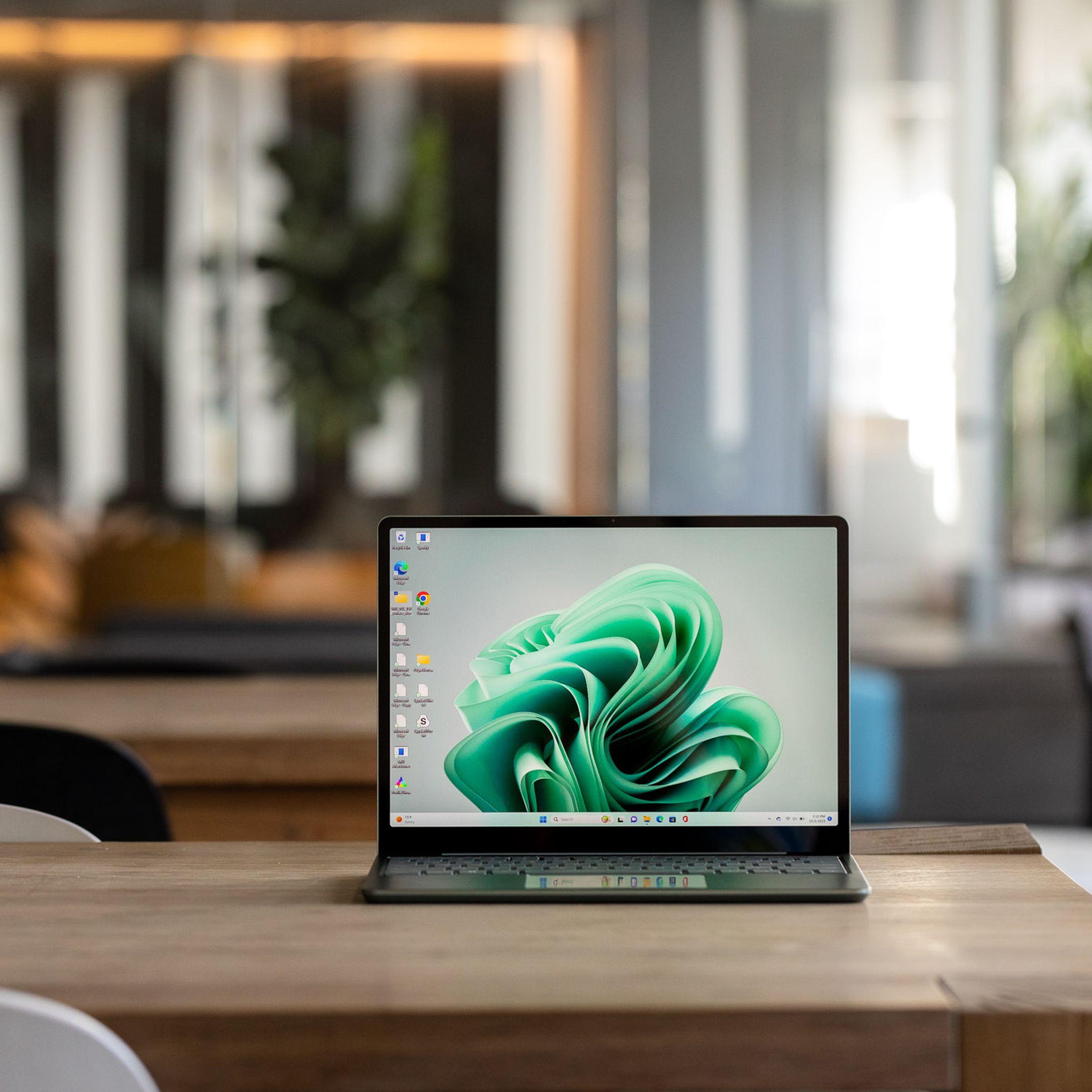 The Microsoft Surface Laptop Go 3 displaying a green Windows desktop on a table in a cafe setting.