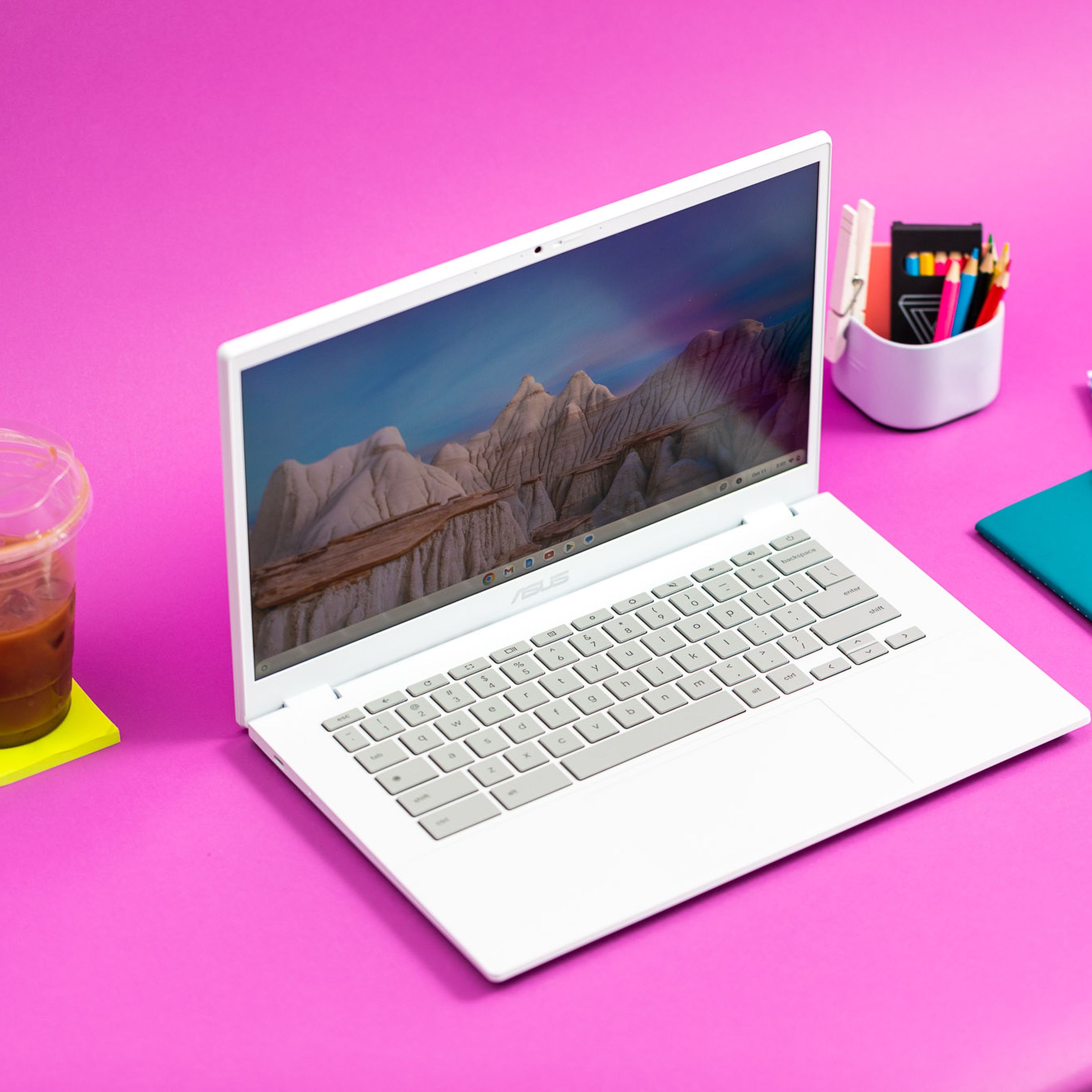 The Asus Chromebook Plus CX34 on a pink table with a coffee and post-it pad beside it.
