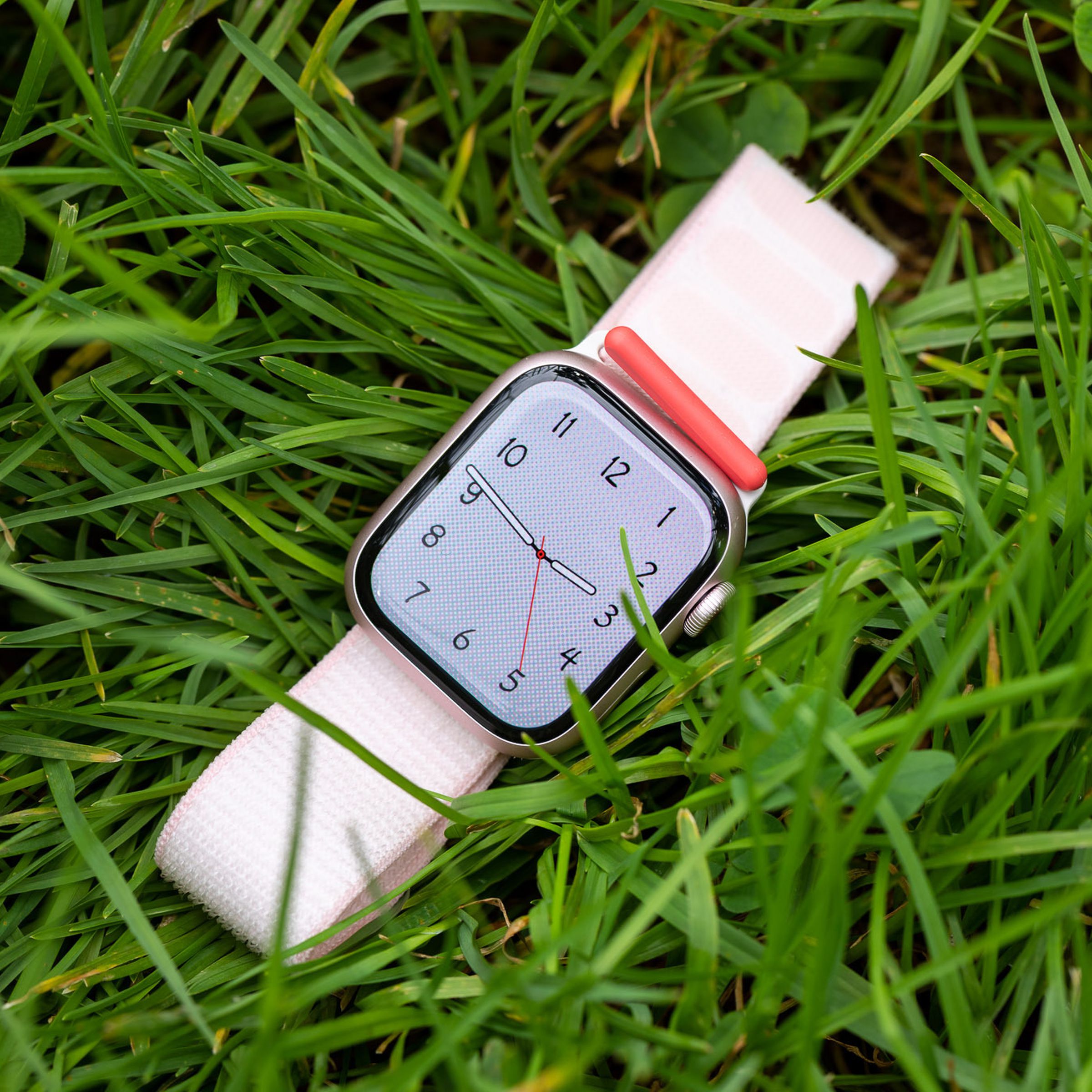 The pink Apple Watch Series 9 lying on grass.