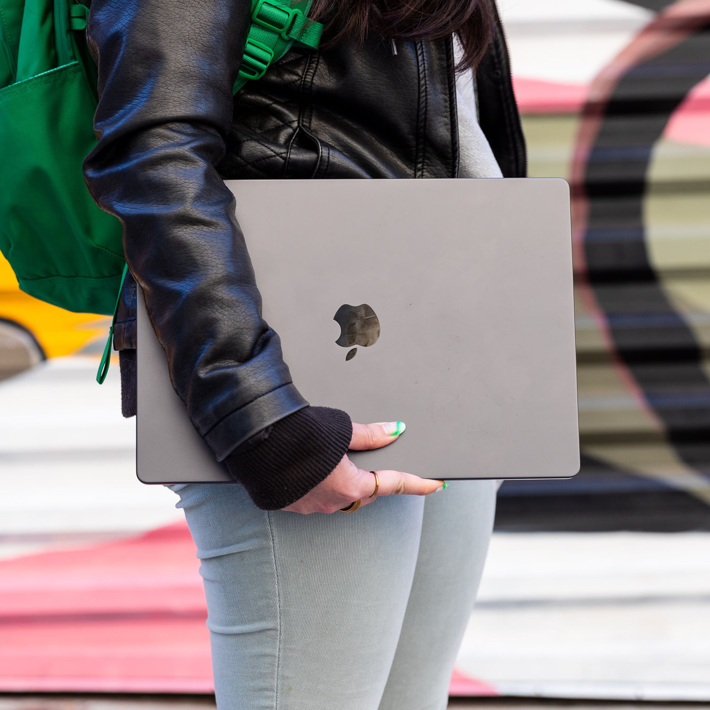 Person holding the M3 Max MacBook Pro 16 in front of a colorful graffiti mural.