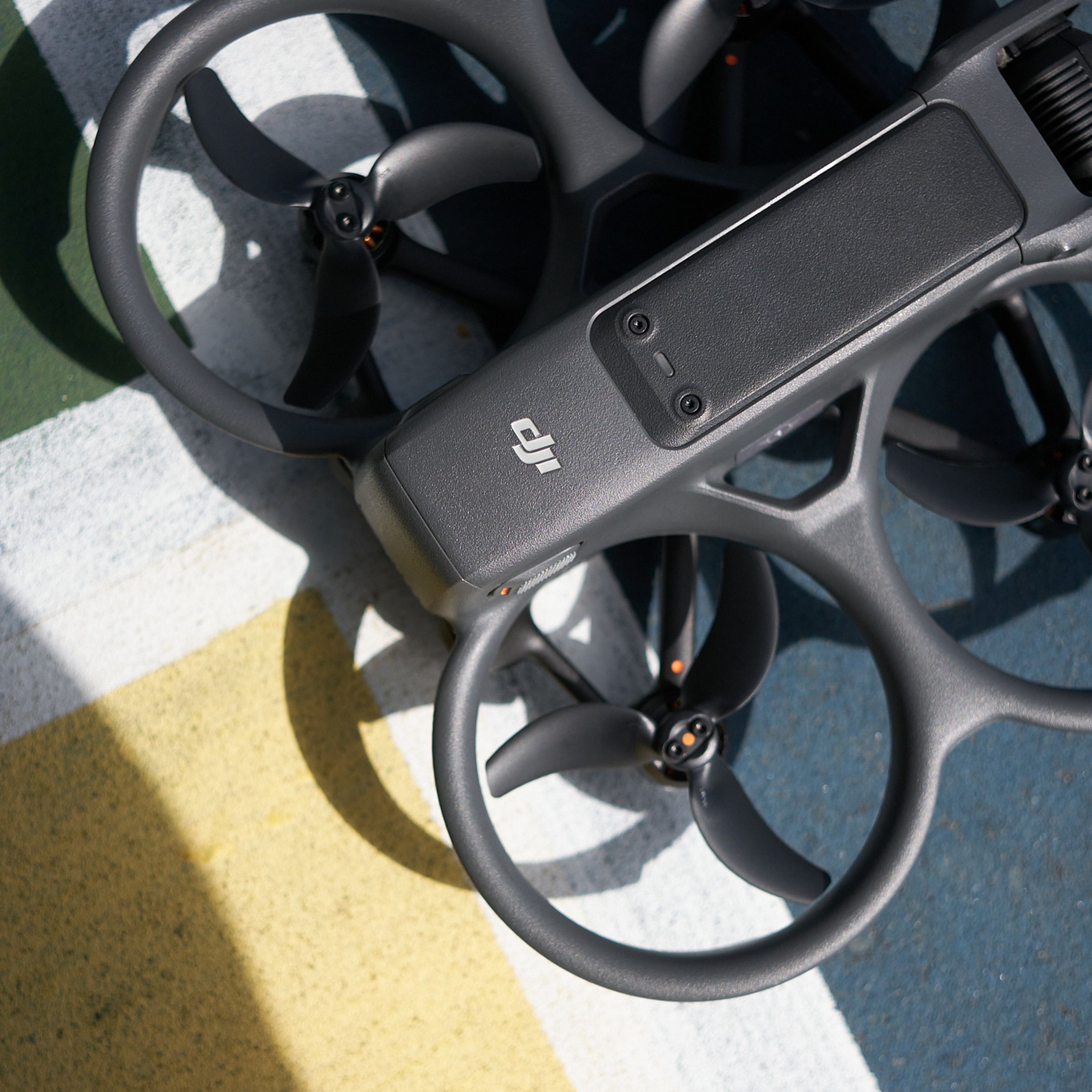 Three-quarters of the image are filled with the frame and three-bladed ducted propellors of a quadcopter drone with a slim gray body and a camera at one end.