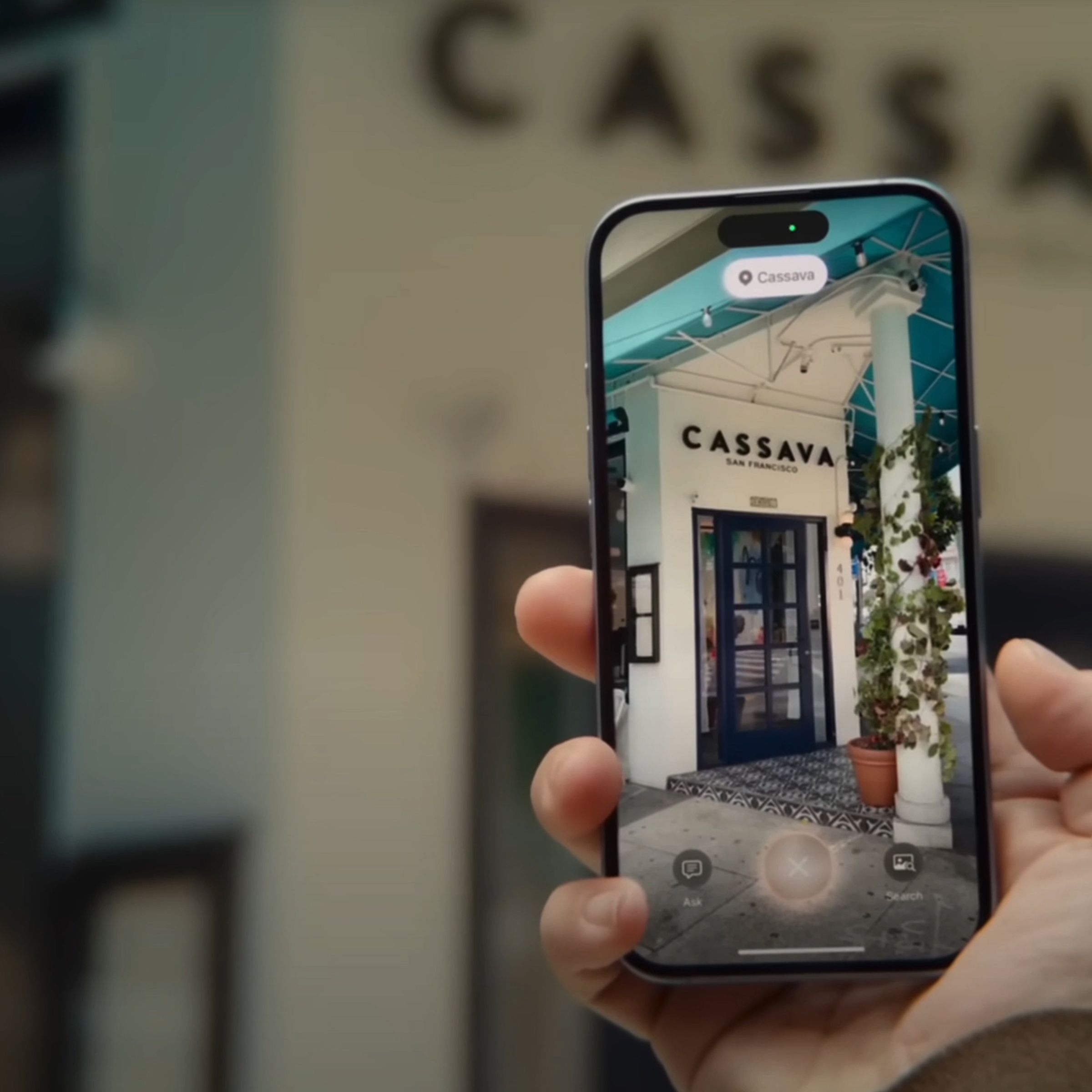 A person using Visual Intelligence from Apple’s iPhone 16 announcement video. The person is holding their iPhone in front of a restaurant and looking at what’s shown onscreen.