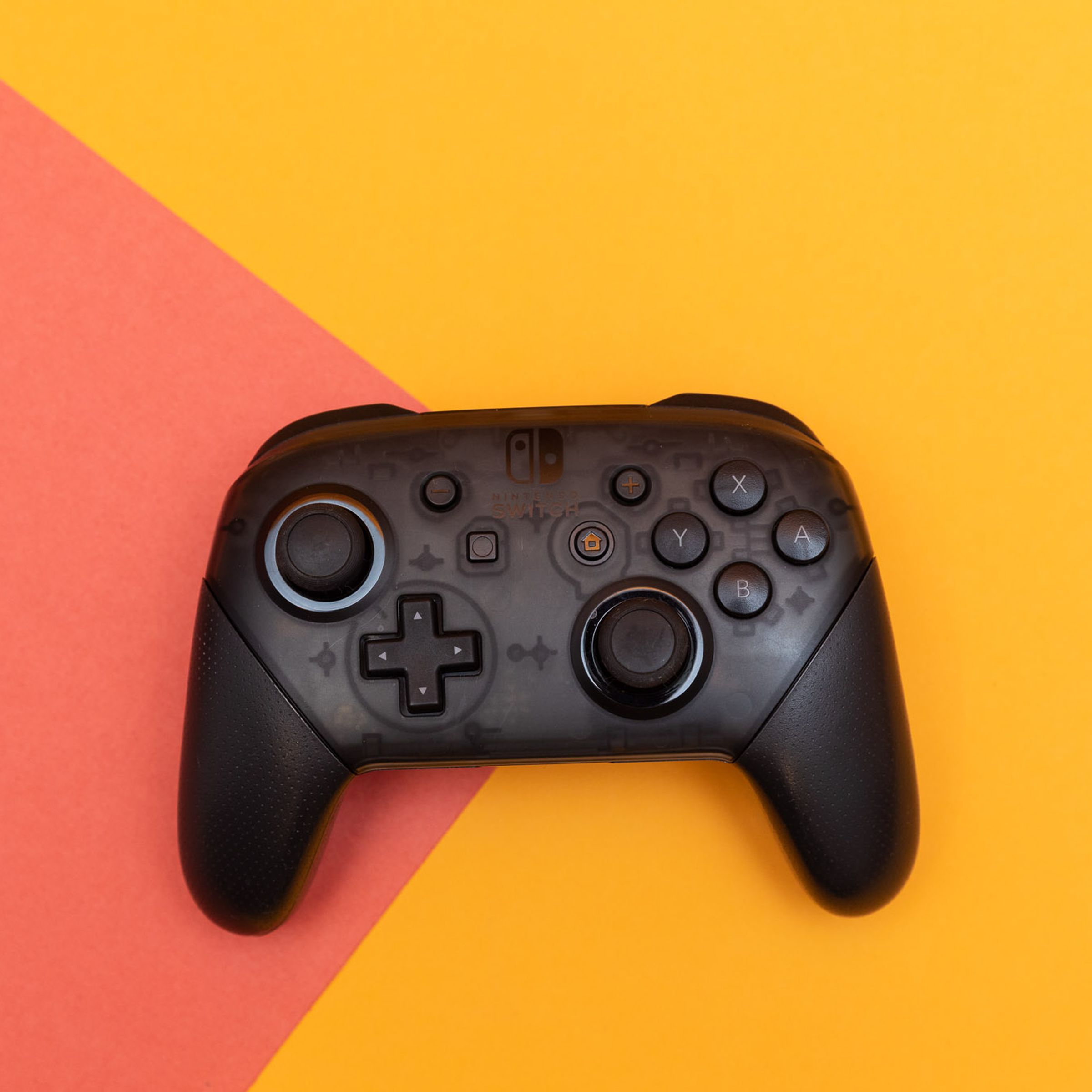 The Nintendo Switch Pro Controller sitting flat on a two-colored backdrop.